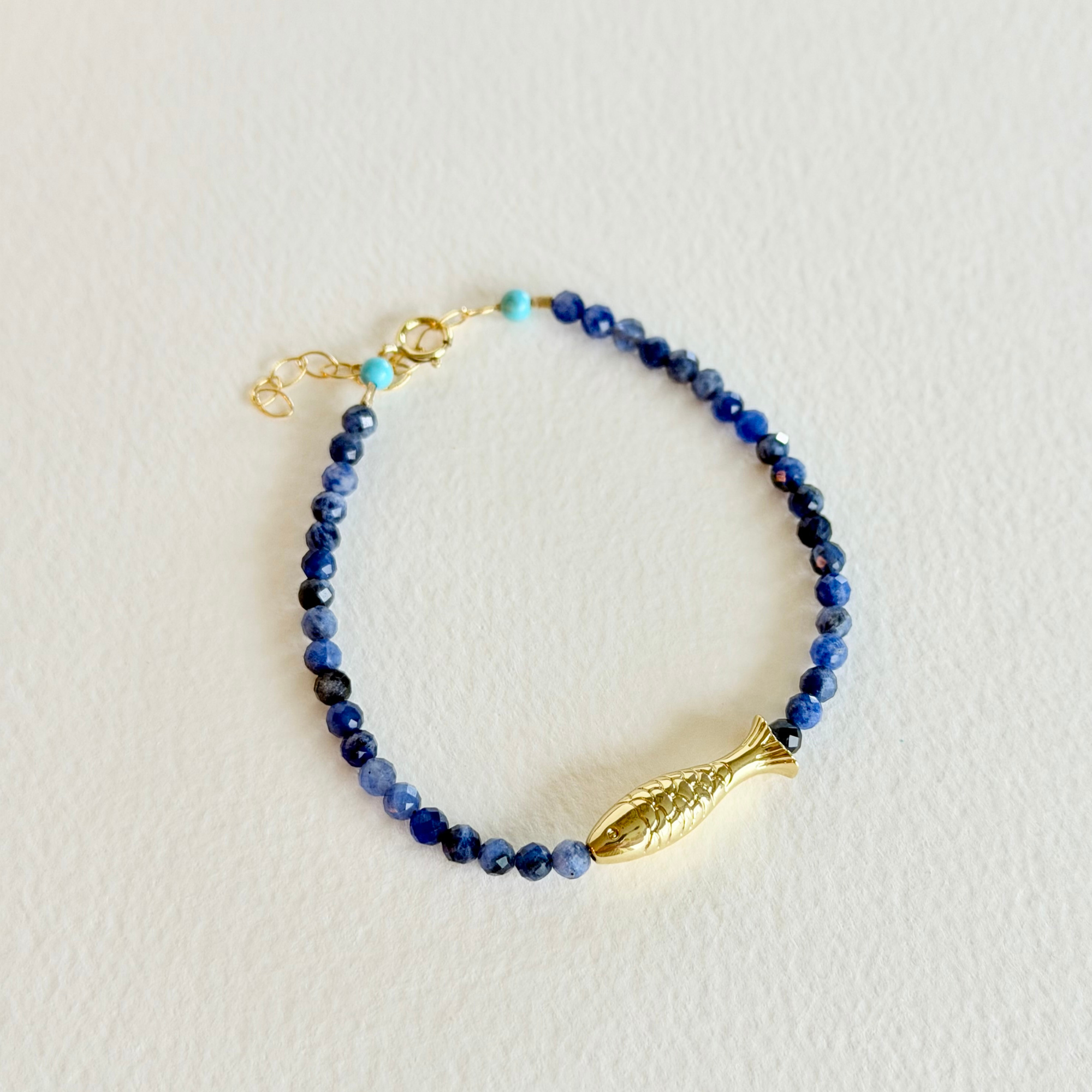 Beaded bracelet with a gold fish charm on a light background