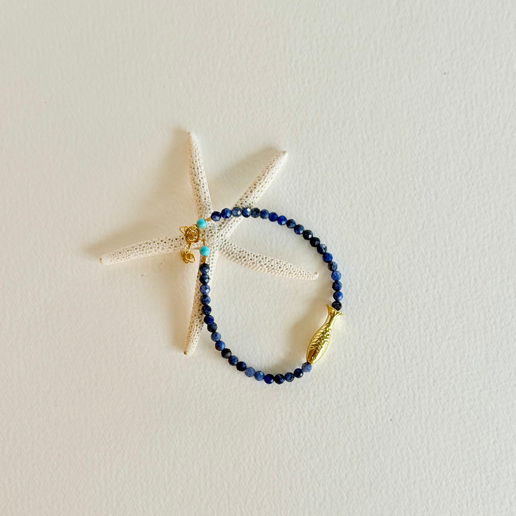 Blue beaded bracelet with gold accents on a starfish against a light background