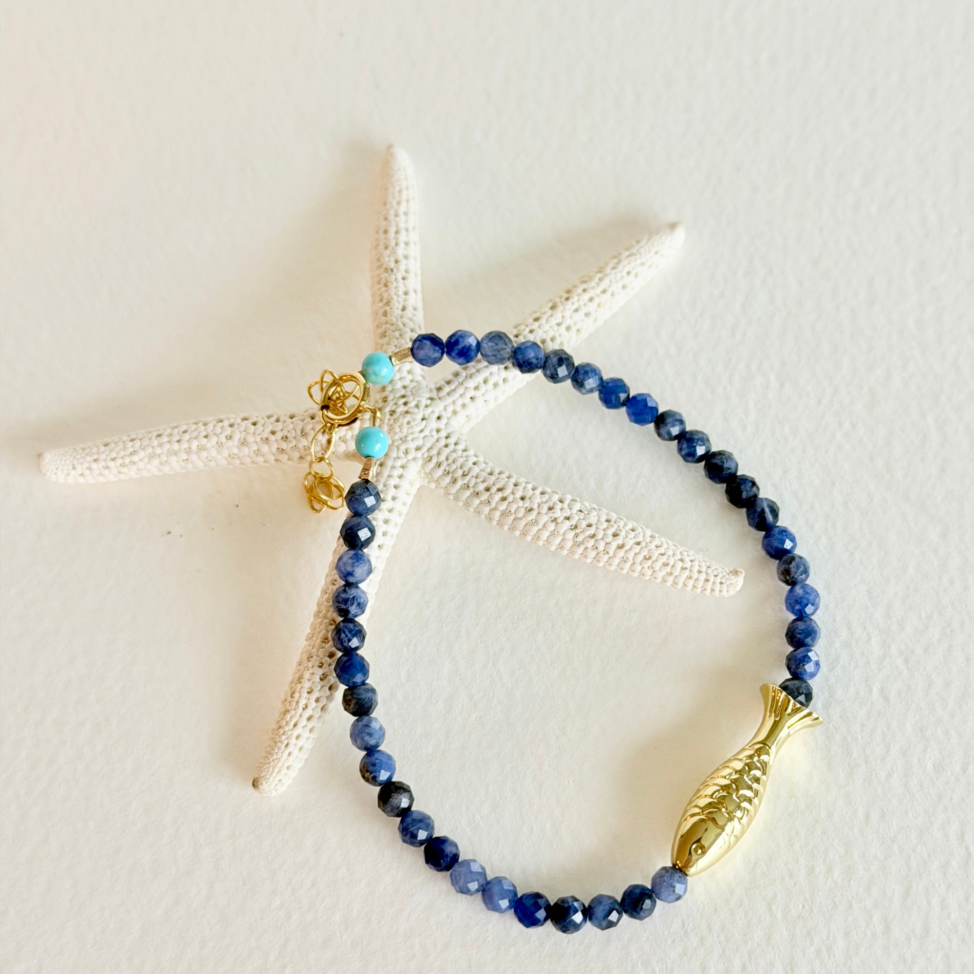 Blue beaded bracelet with gold fish charm on a starfish
