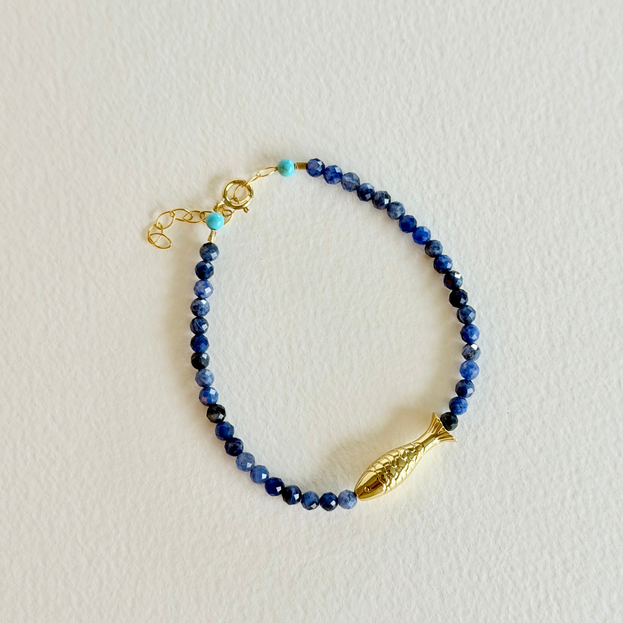Blue beaded bracelet with a gold fish charm on a light gray background