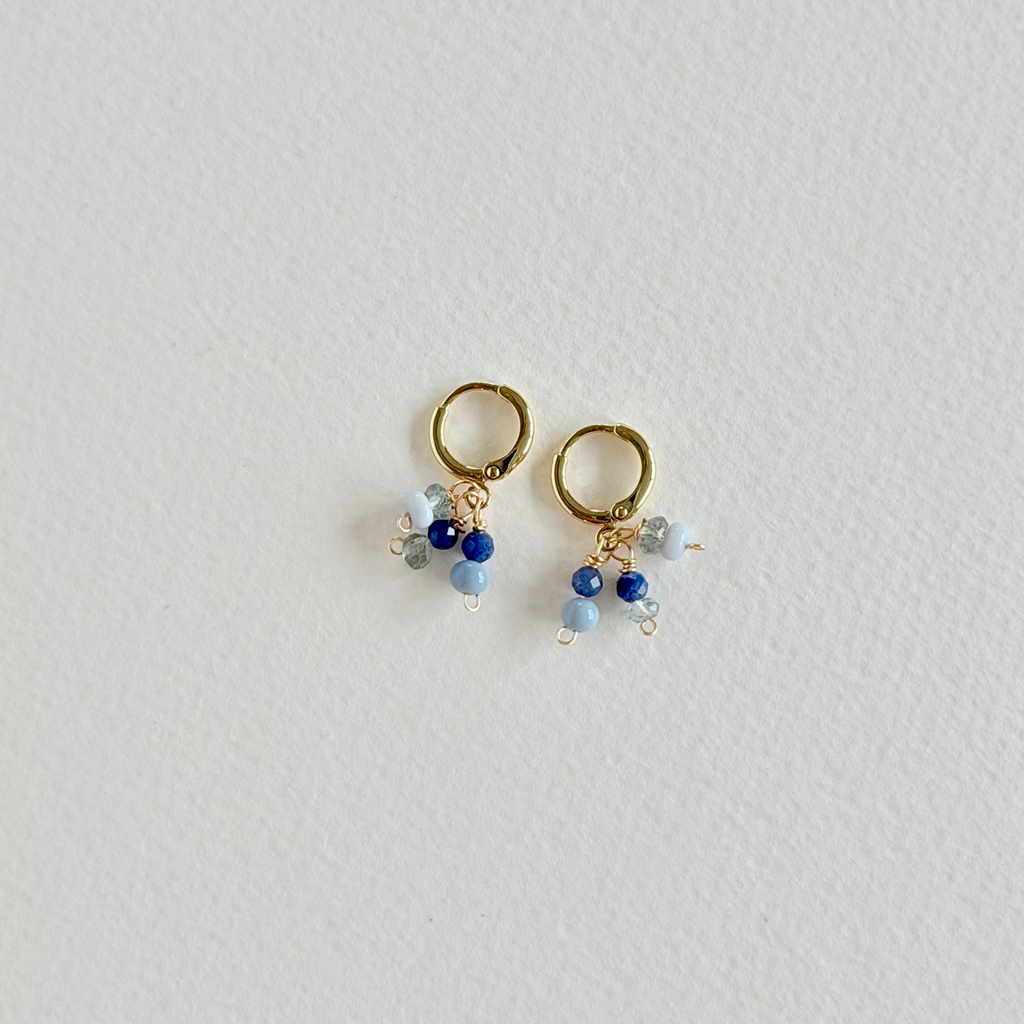 Pair of gold hoop earrings with blue and clear bead charms on a light gray background