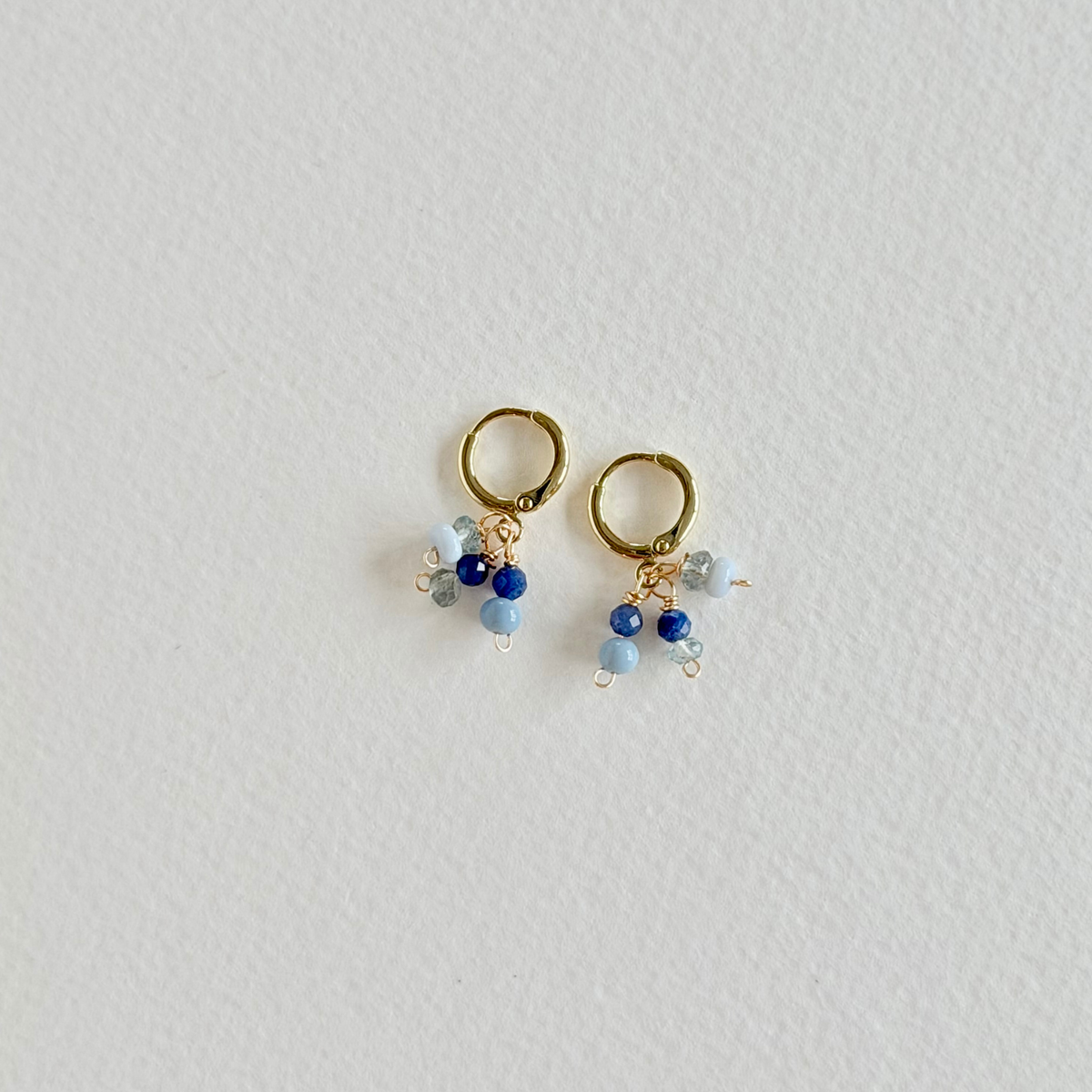 Pair of gold hoop earrings with blue and clear bead charms on a light gray background