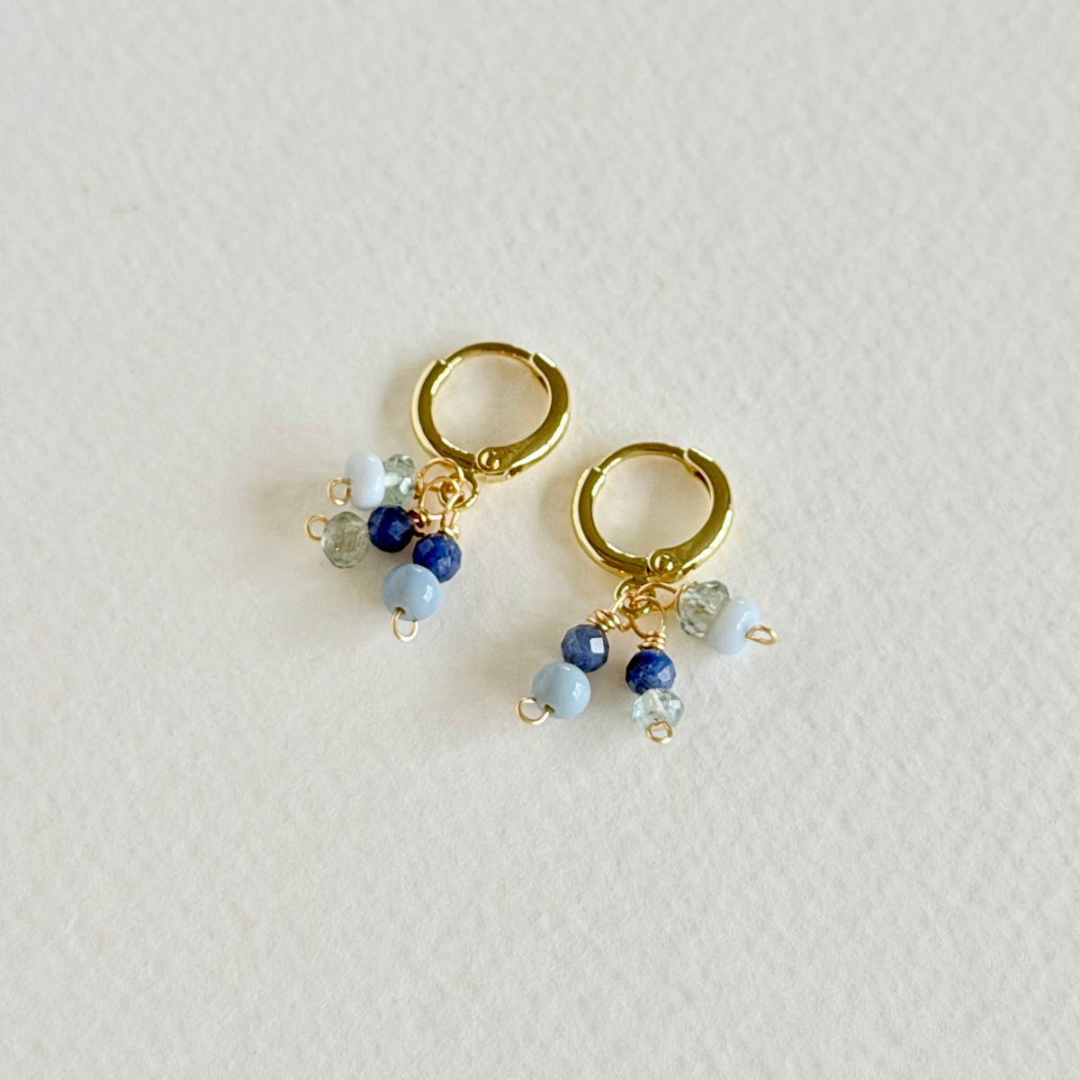 Gold hoop earrings with blue and clear bead charms on a light gray background
