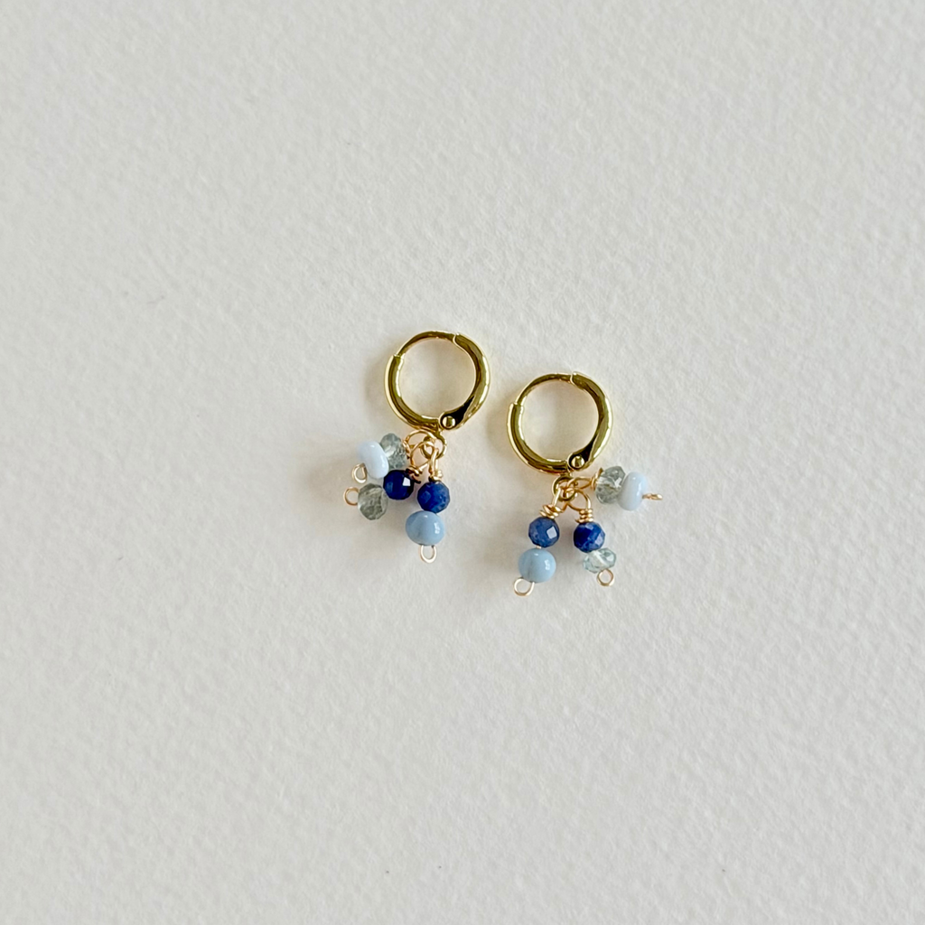 Gold hoop earrings with blue and clear beads on a light gray background