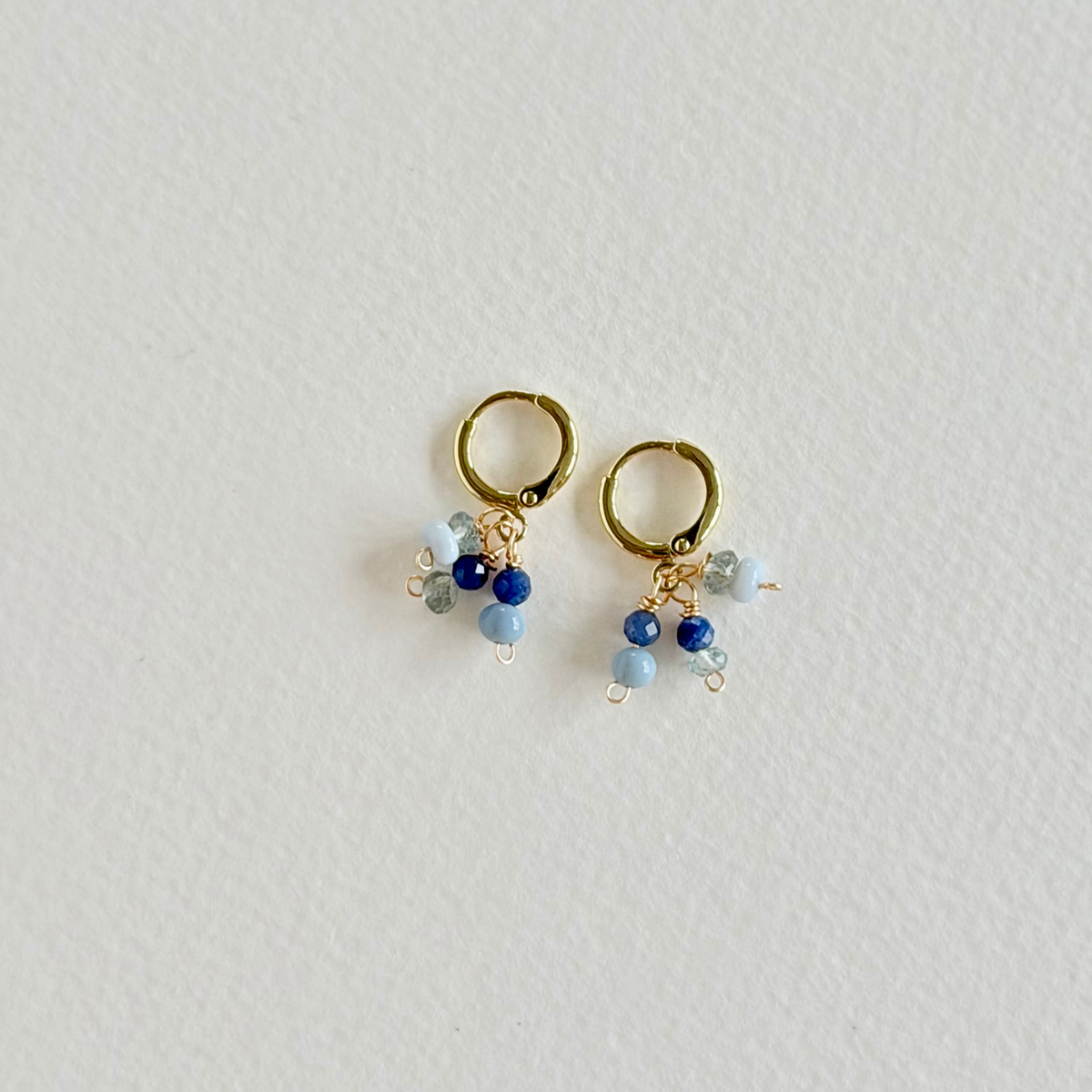 Gold hoop earrings with blue and clear beads on a light gray background