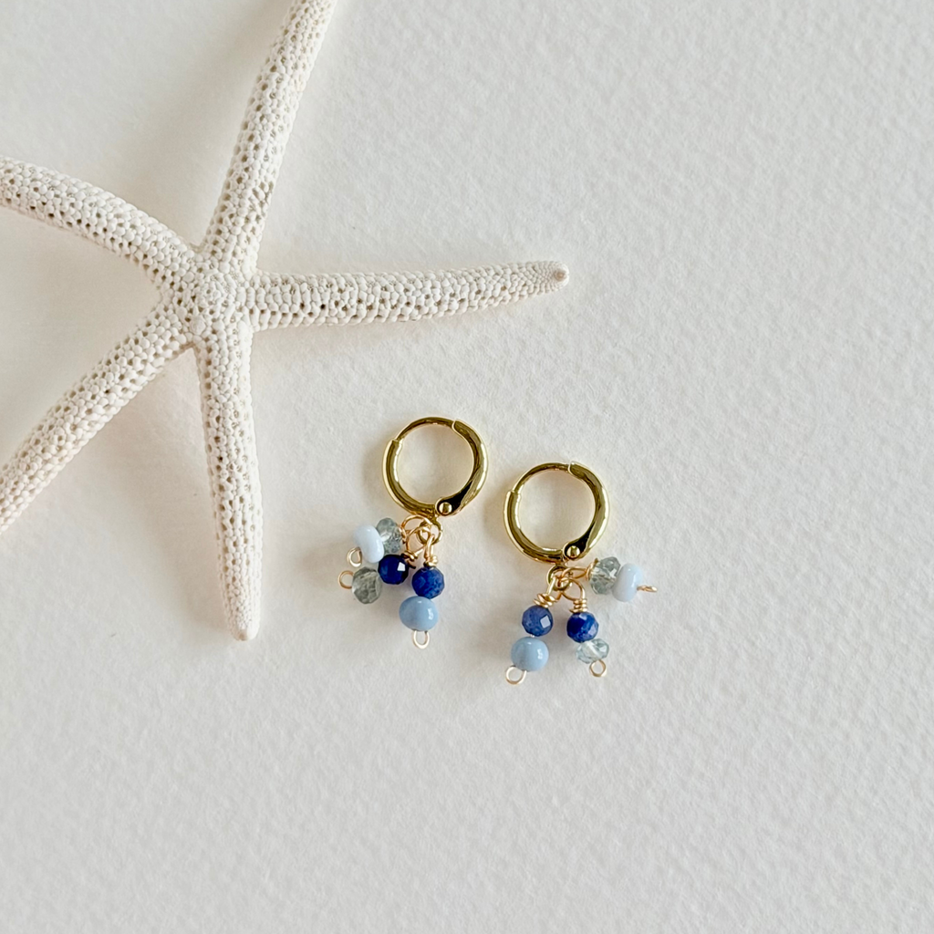 Gold hoop earrings with blue beads on a white surface with a starfish.