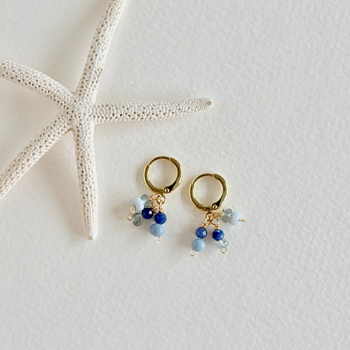 Gold hoop earrings with blue beads on a white surface with a starfish.