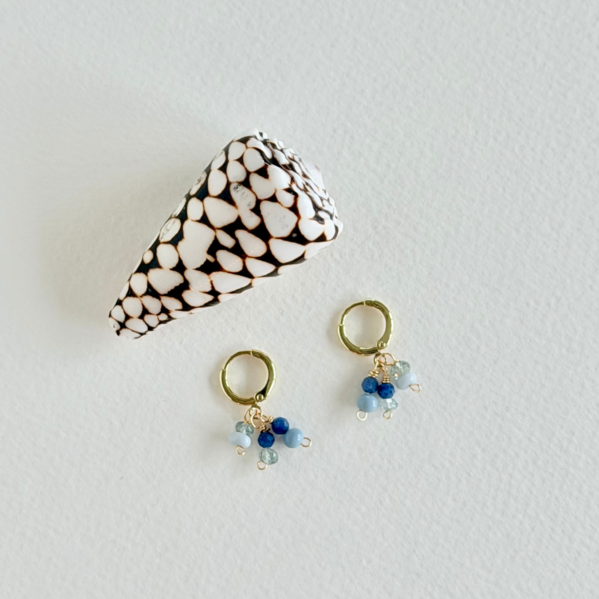 Pair of gold earrings with blue beads on a light gray background