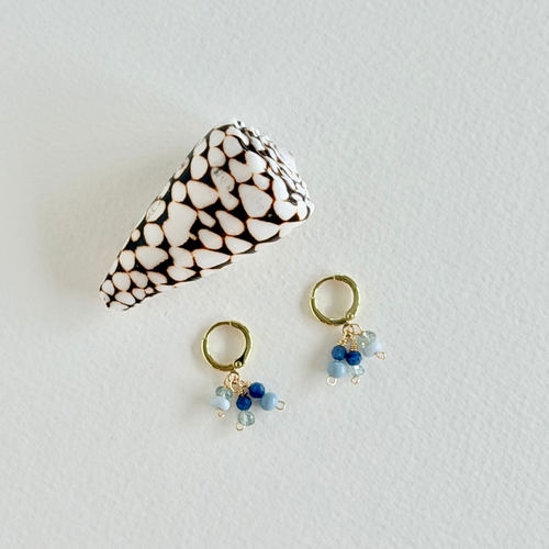 Pair of gold earrings with blue beads on a light gray background