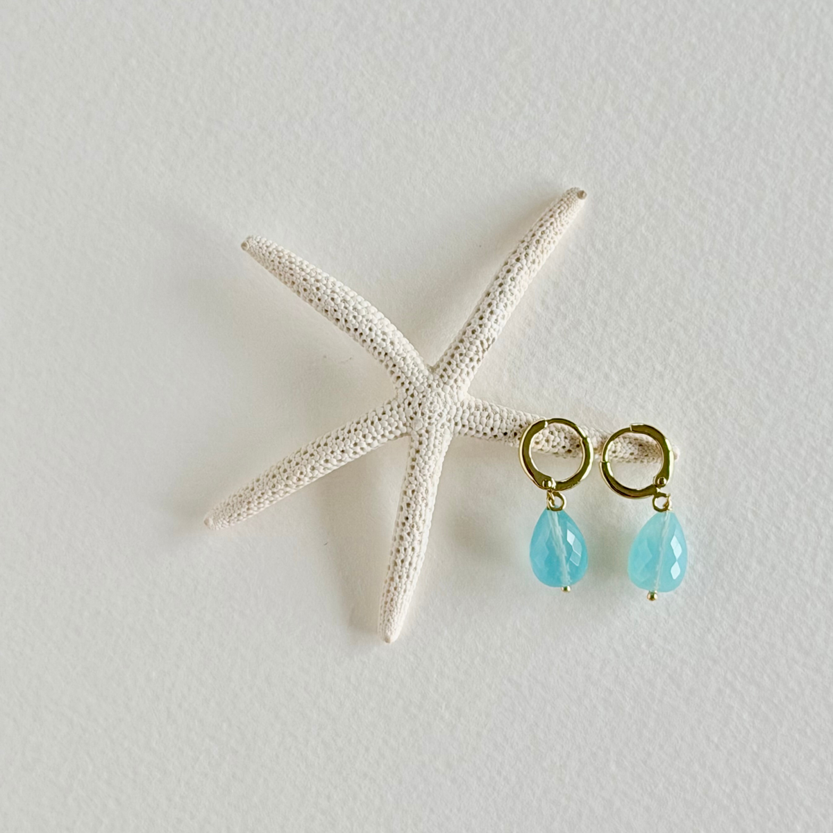 Turquoise teardrop earrings with gold hooks on a starfish against a light background