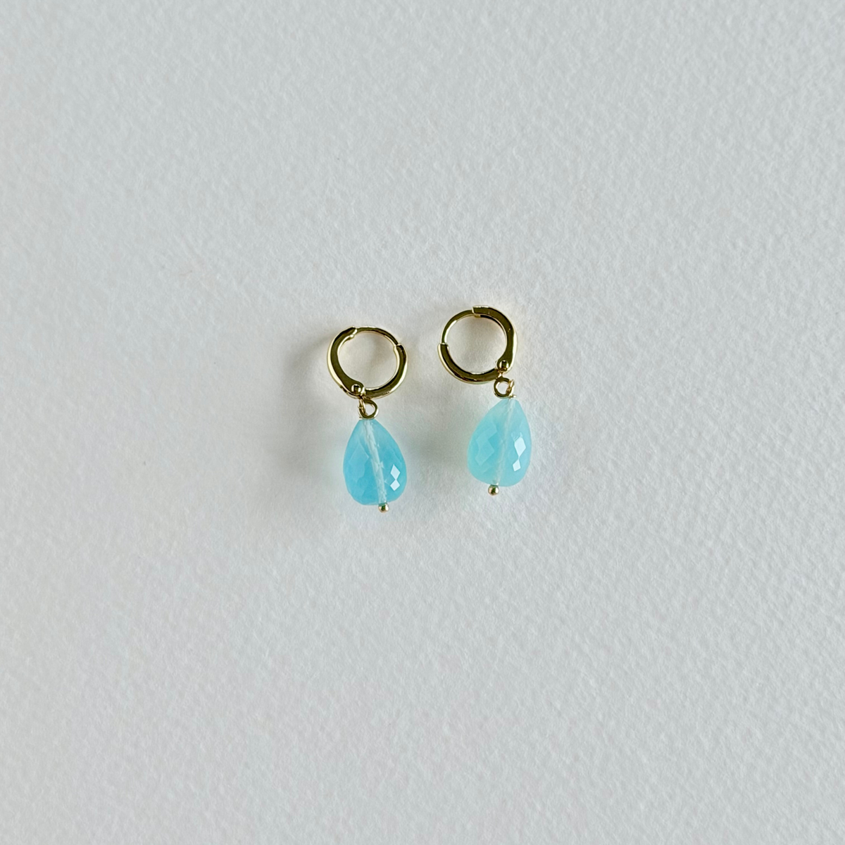 Pair of gold earrings with turquoise teardrop stones on a light gray background