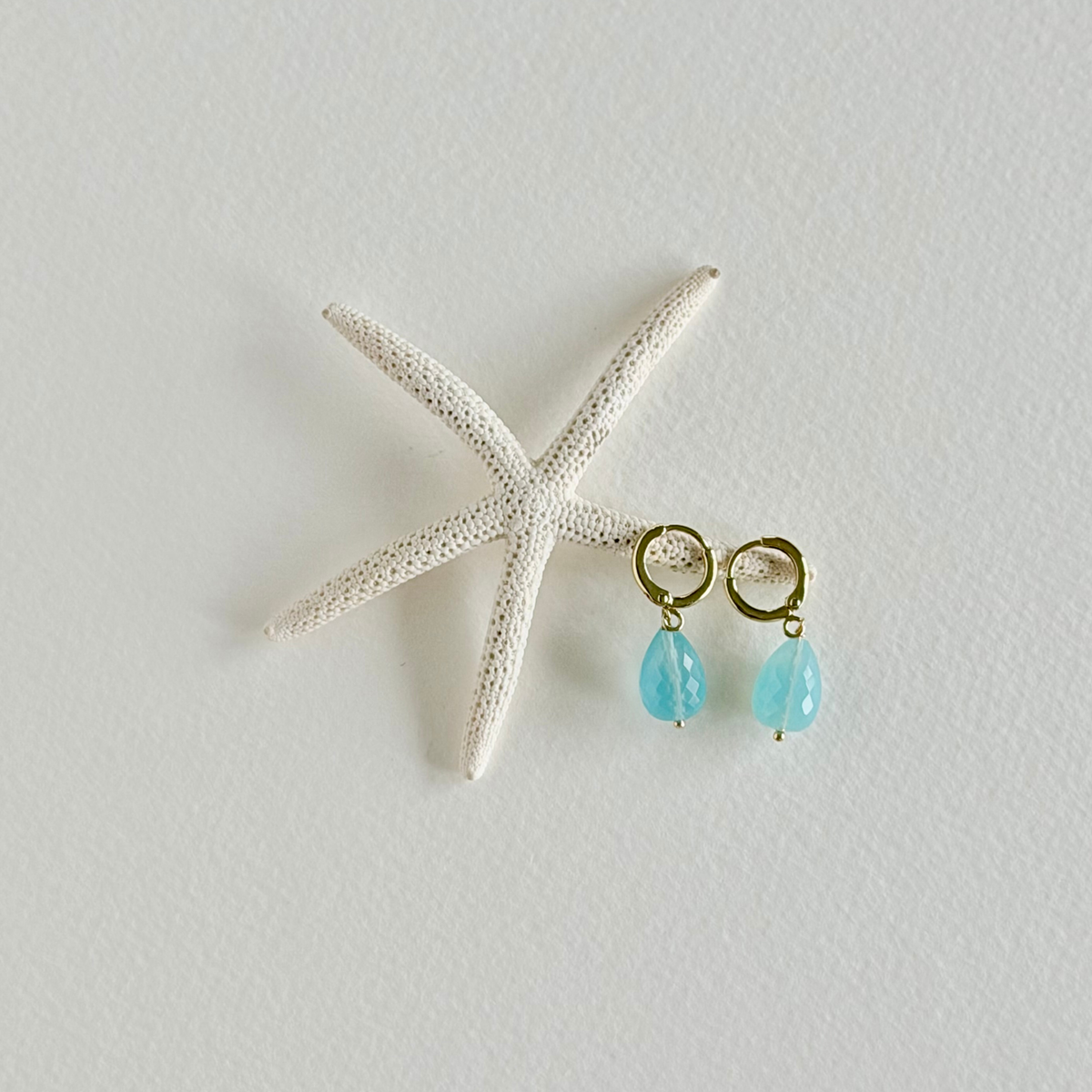 Turquoise earrings with gold hooks on a starfish against a light background