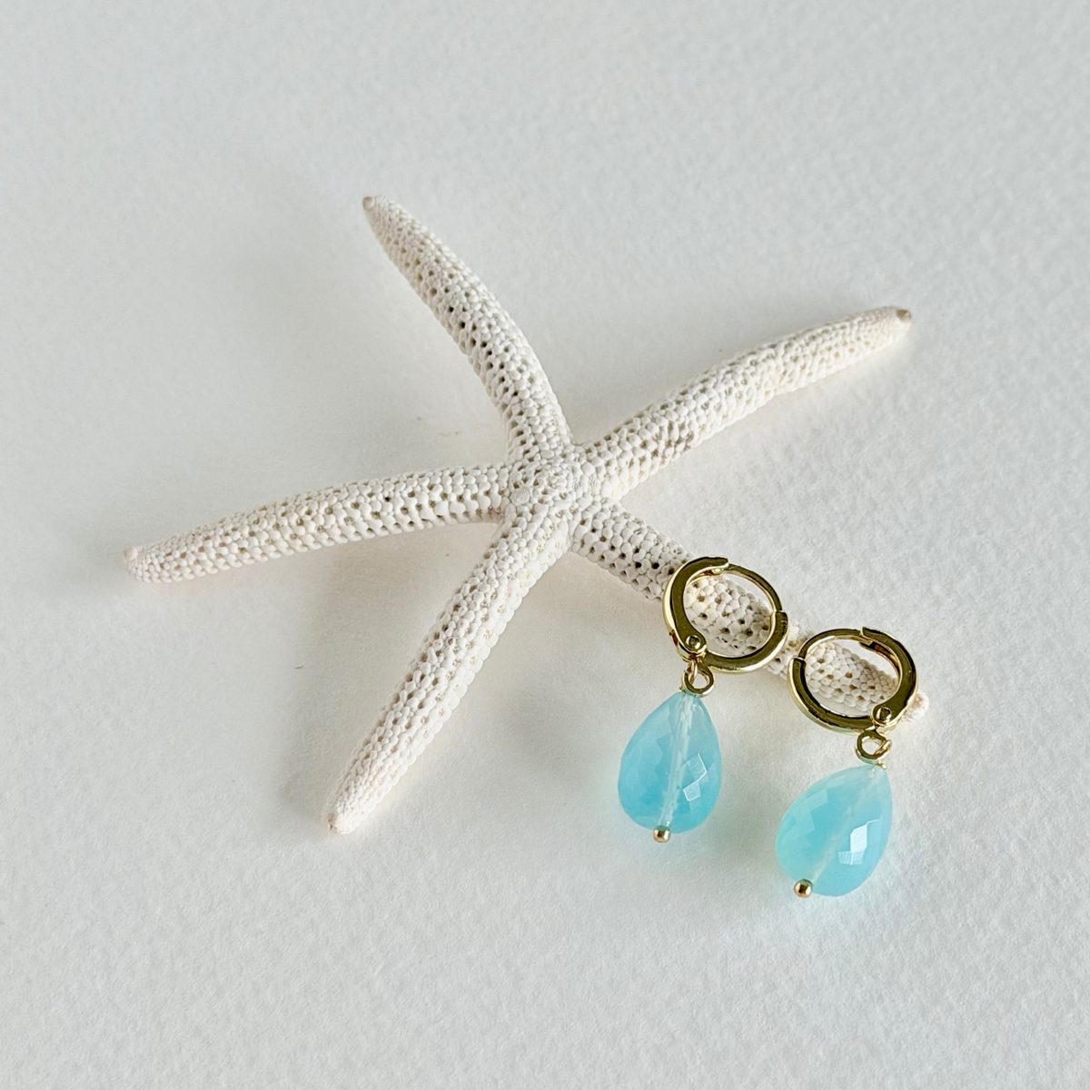 Turquoise teardrop earrings with gold hooks on a starfish against a light gray background