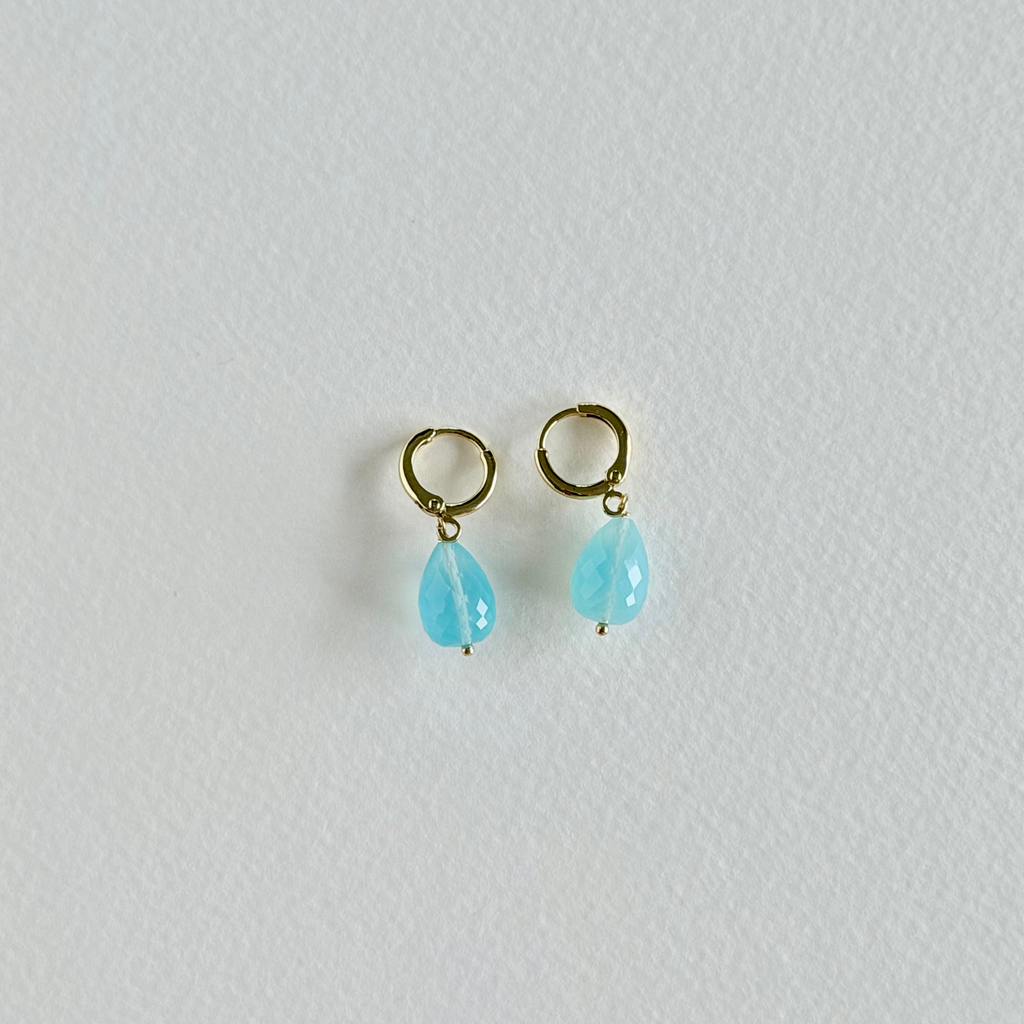 Pair of gold earrings with turquoise teardrop stones on a light gray background