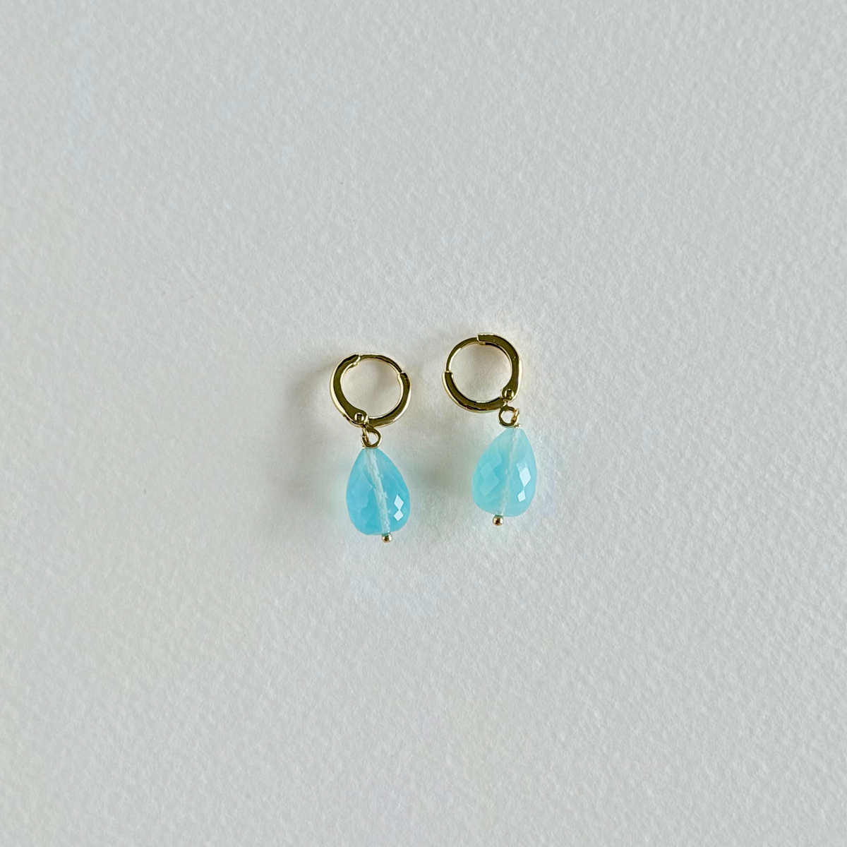 Pair of gold earrings with turquoise teardrop stones on a light gray background