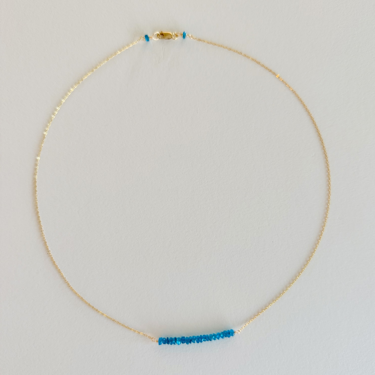 Gold necklace with a blue bar pendant on a light gray background
