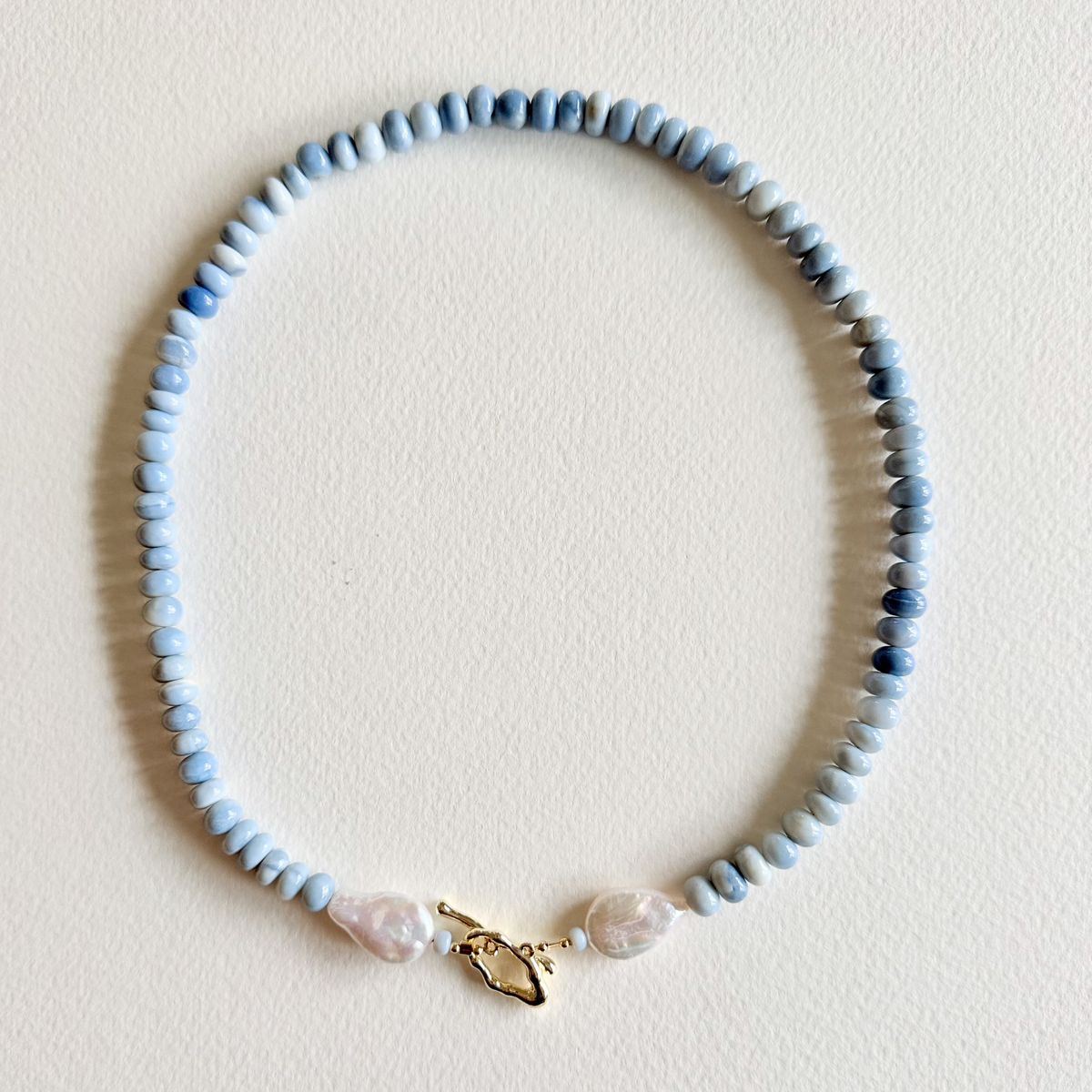 Necklace with blue beads and a gold clasp on a light background