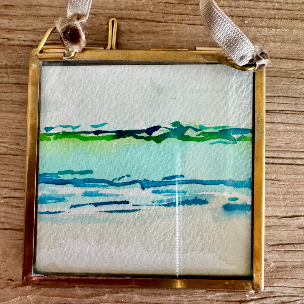 Watercolor of abstract seascape in tan, blue, and green. Framed in brass square glass frame and tied with brown velvet ribbon to hang as an ornament.
