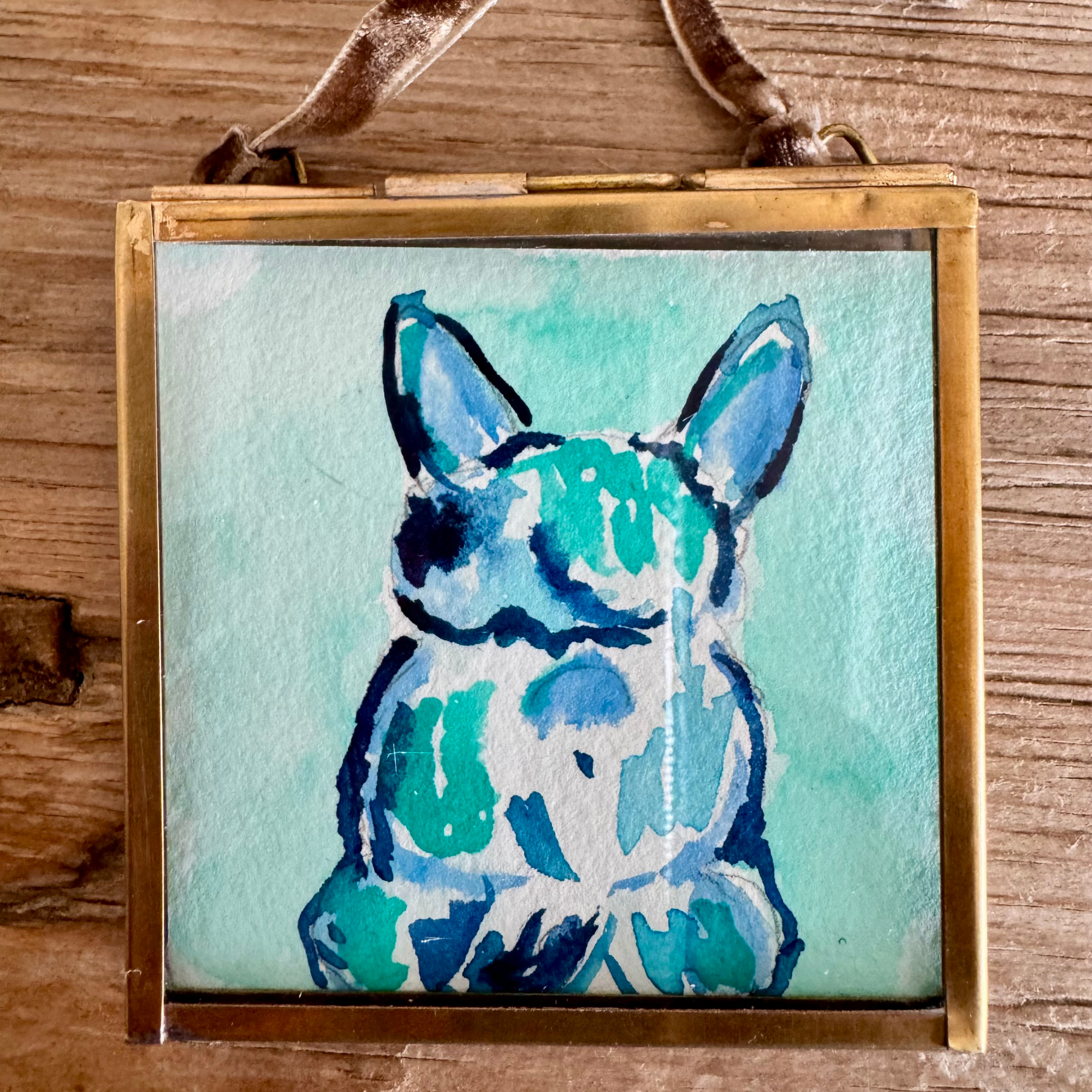 Watercolor of bulldog in turquoise, blue, and green. Framed in brass square glass frame and tied with brown velvet ribbon to hang as an ornament.