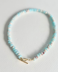 A beaded bracelet with light blue, white, and pink marbled beads, finished with a gold toggle clasp, displayed on a light gray textured surface.