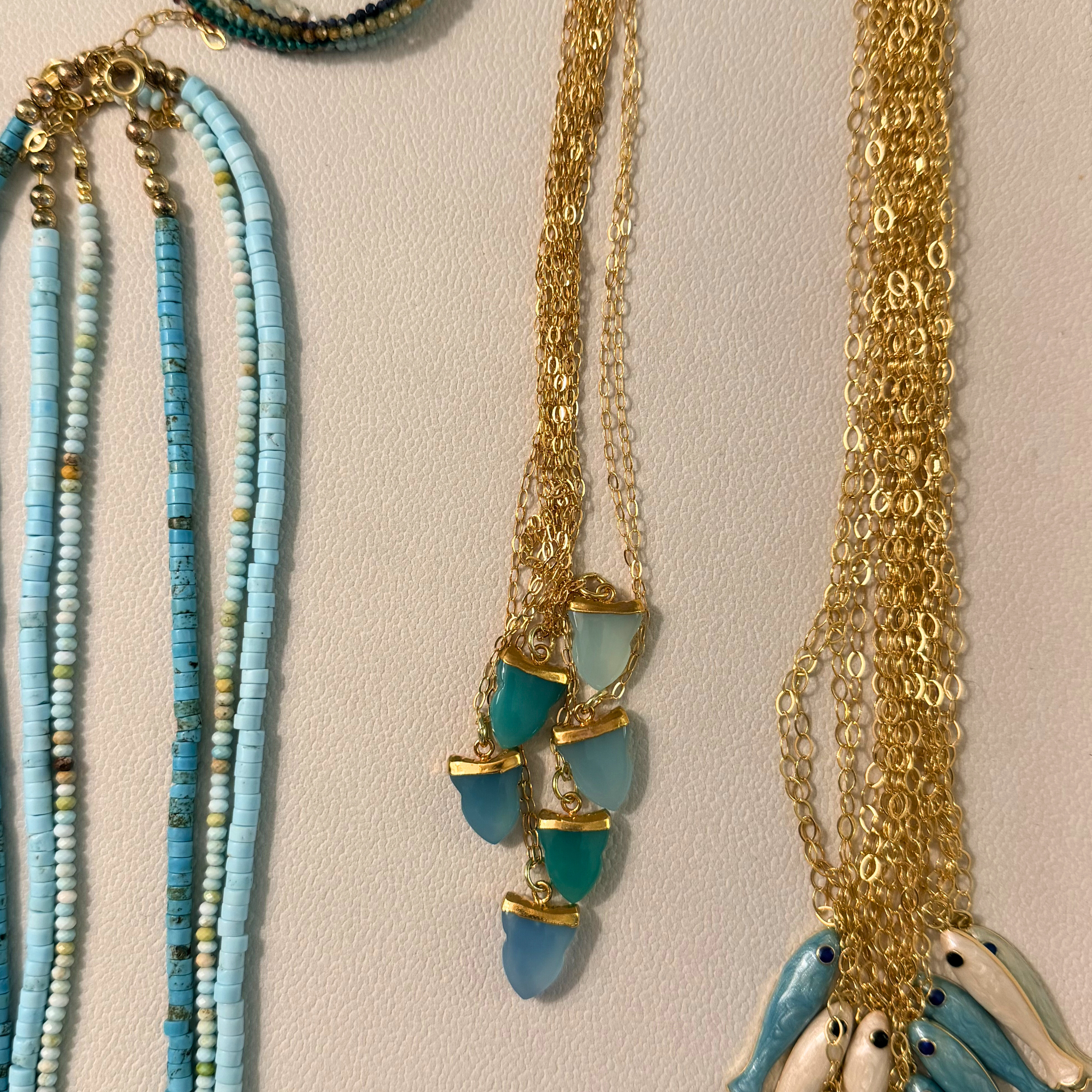 Three necklaces with blue beads and gold chains on a beige background