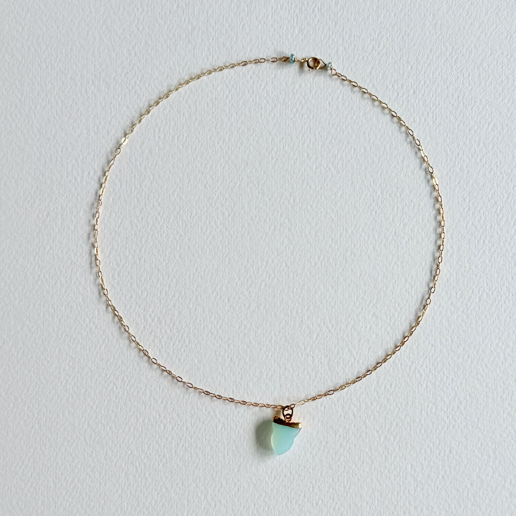 Gold necklace with a turquoise pendant on a light gray background