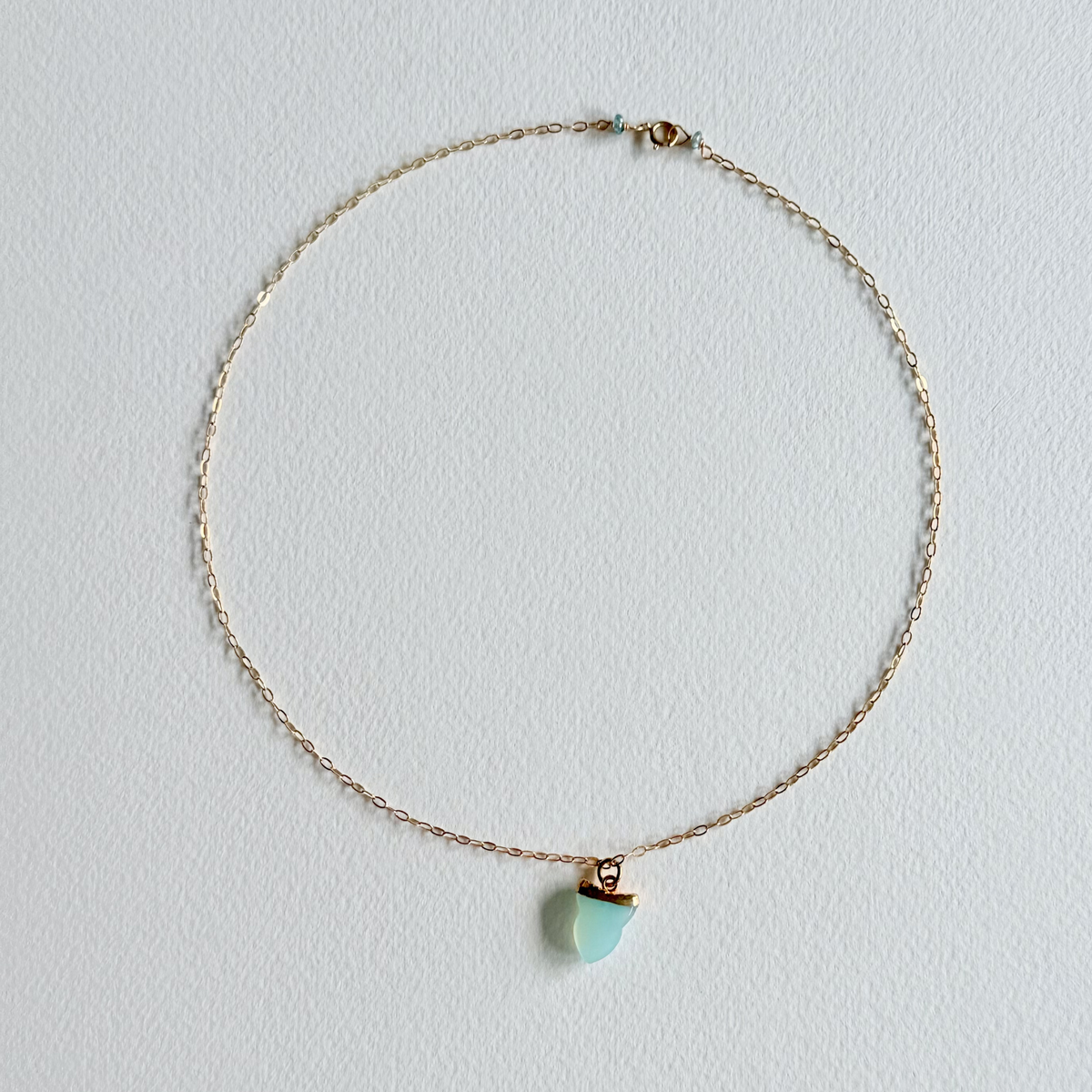 Gold necklace with a turquoise pendant on a light gray background