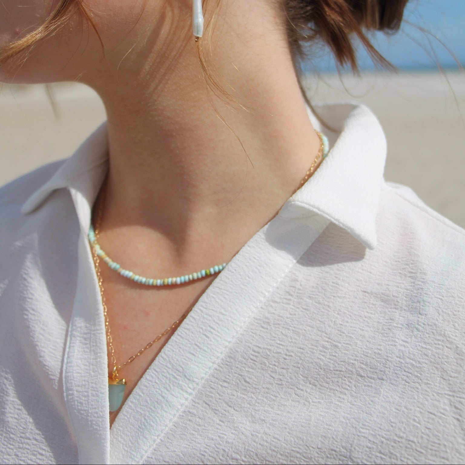 Close-up of a person wearing earrings with a blurred beach background