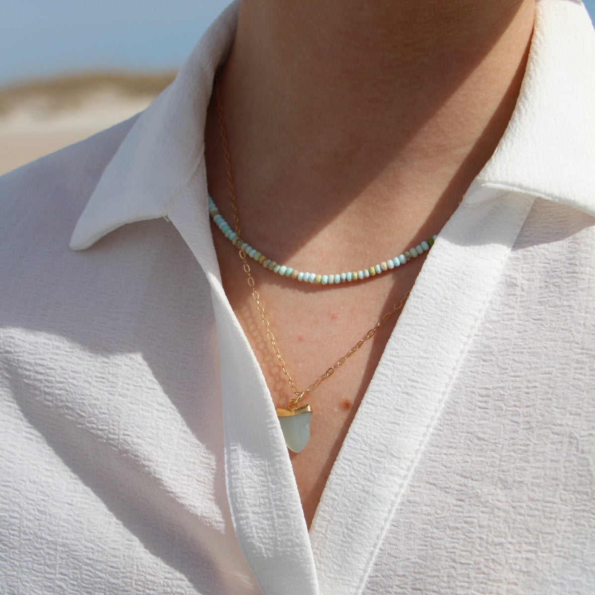 Close-up of a person wearing a white shirt with a necklace and earrings.