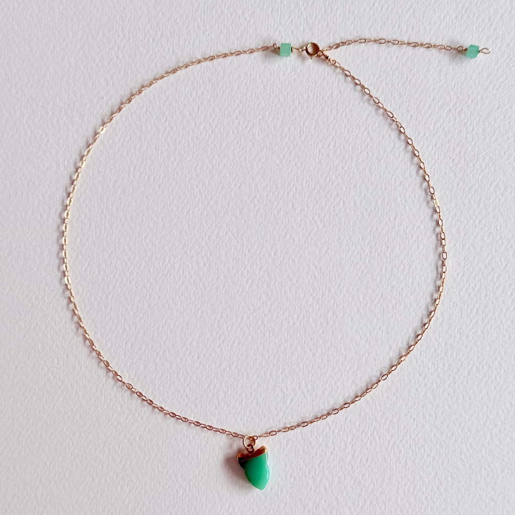 gold necklace with a green pendant on a light gray background
