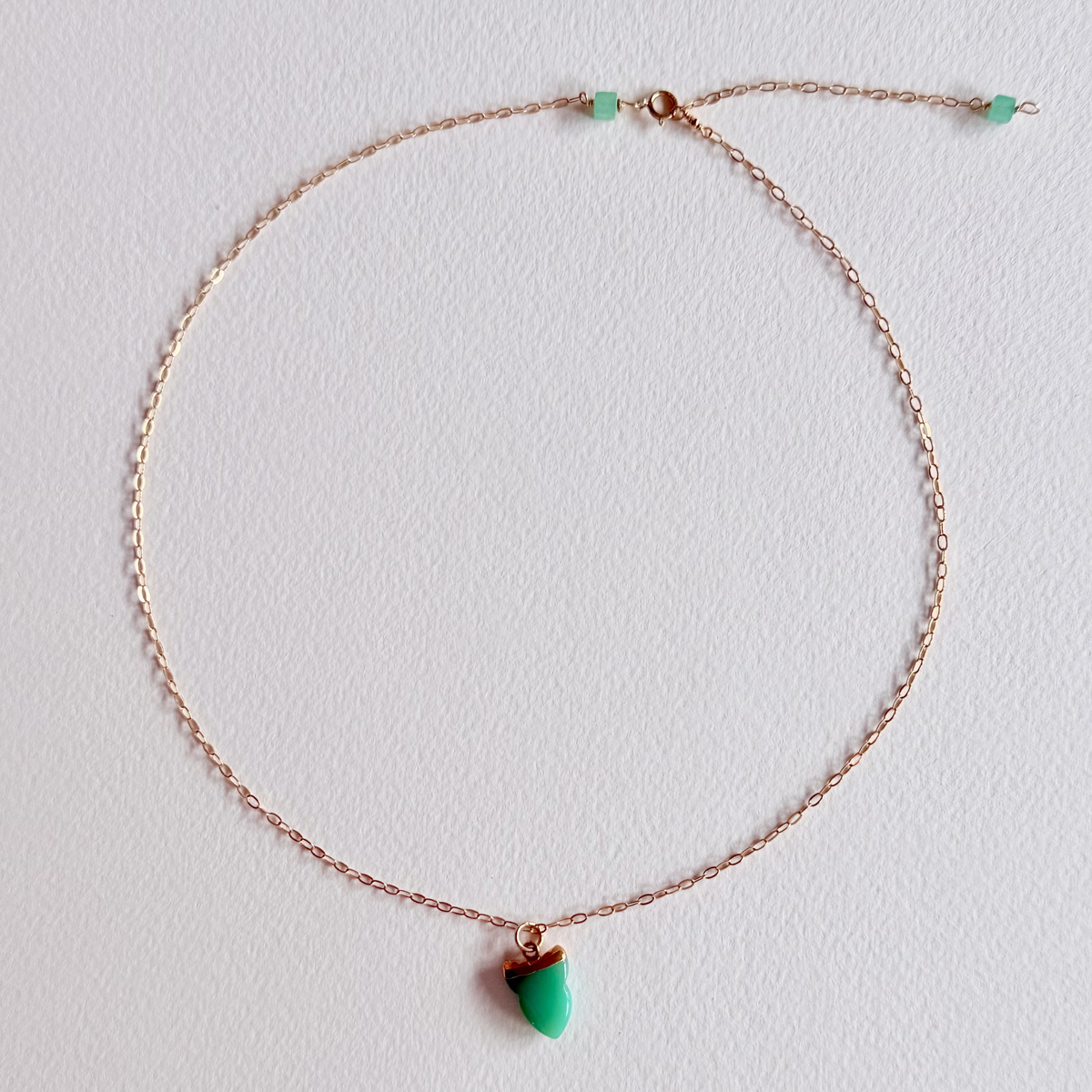 gold necklace with a green pendant on a light gray background