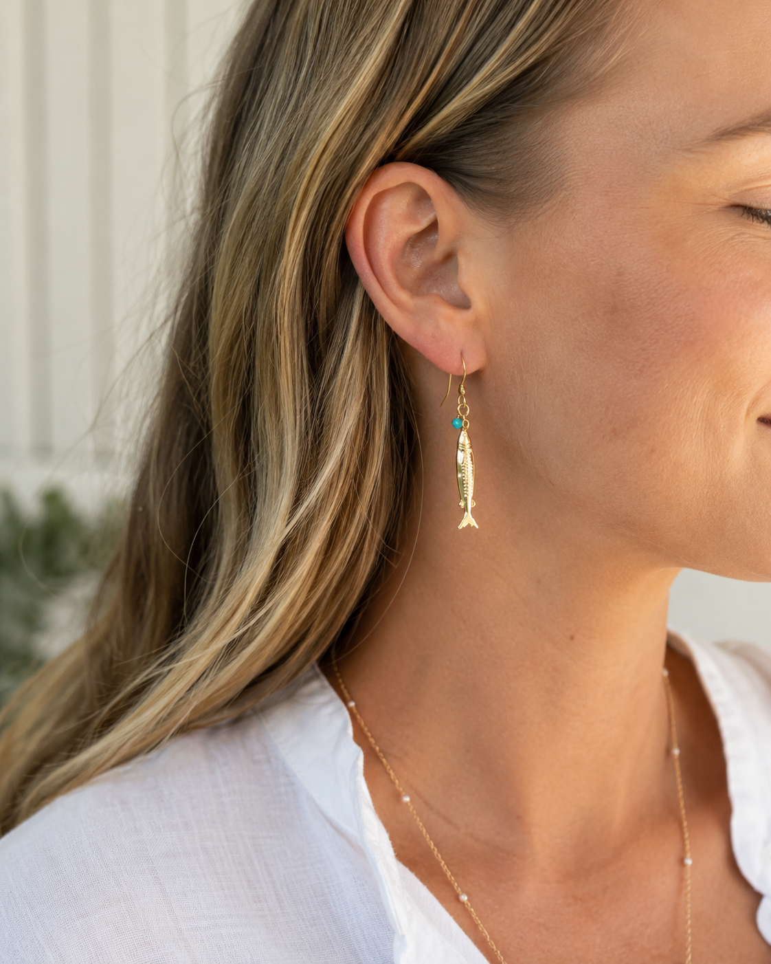 Close-up of a woman wearing gold fish-shaped earrings with a blurred background