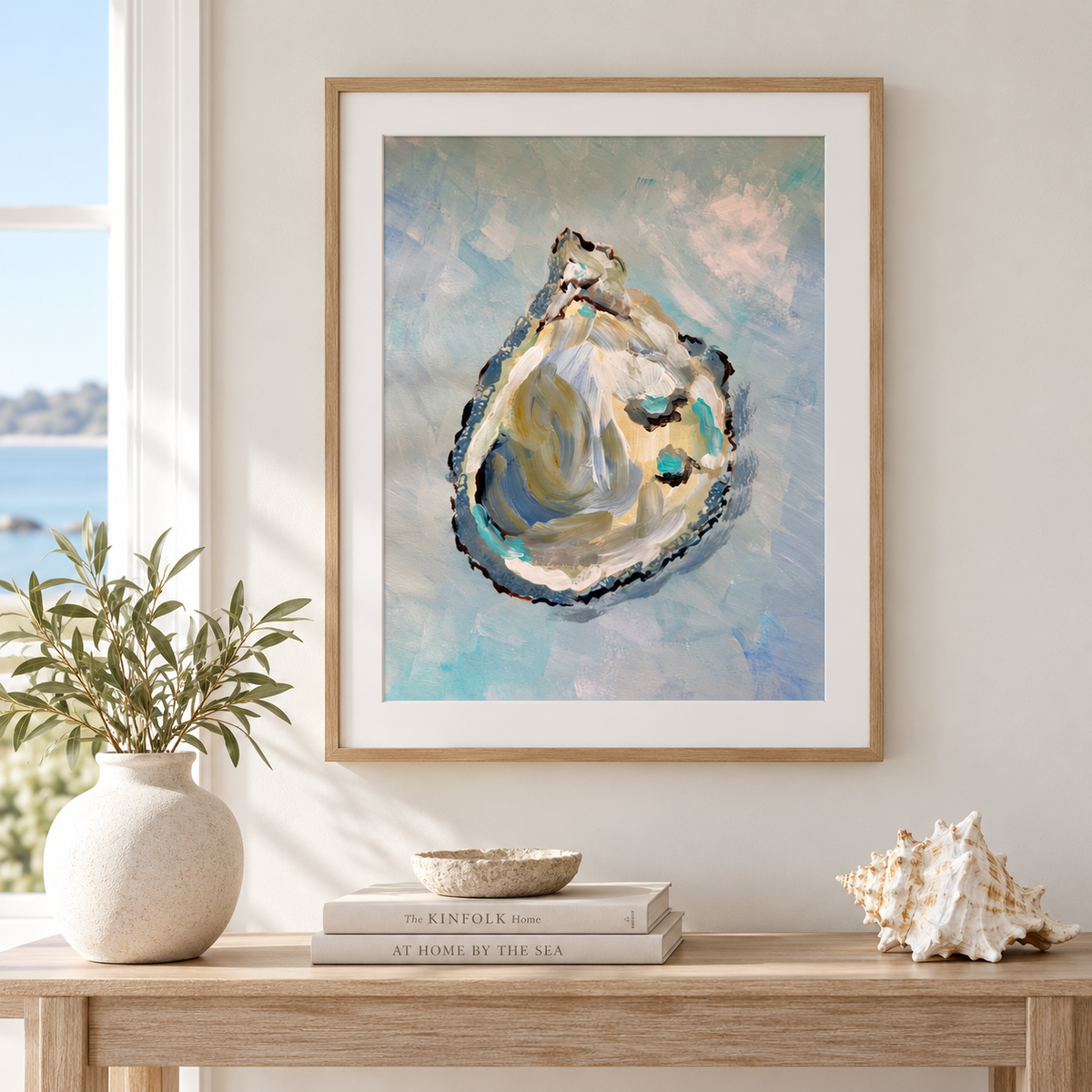 Framed wall art featuring an artistic depiction of an oyster shell, styled on a light wood console table in a bright room with a vase of greenery and a seashell.