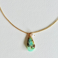 Turquoise pendant necklace on a gold chain against a white background