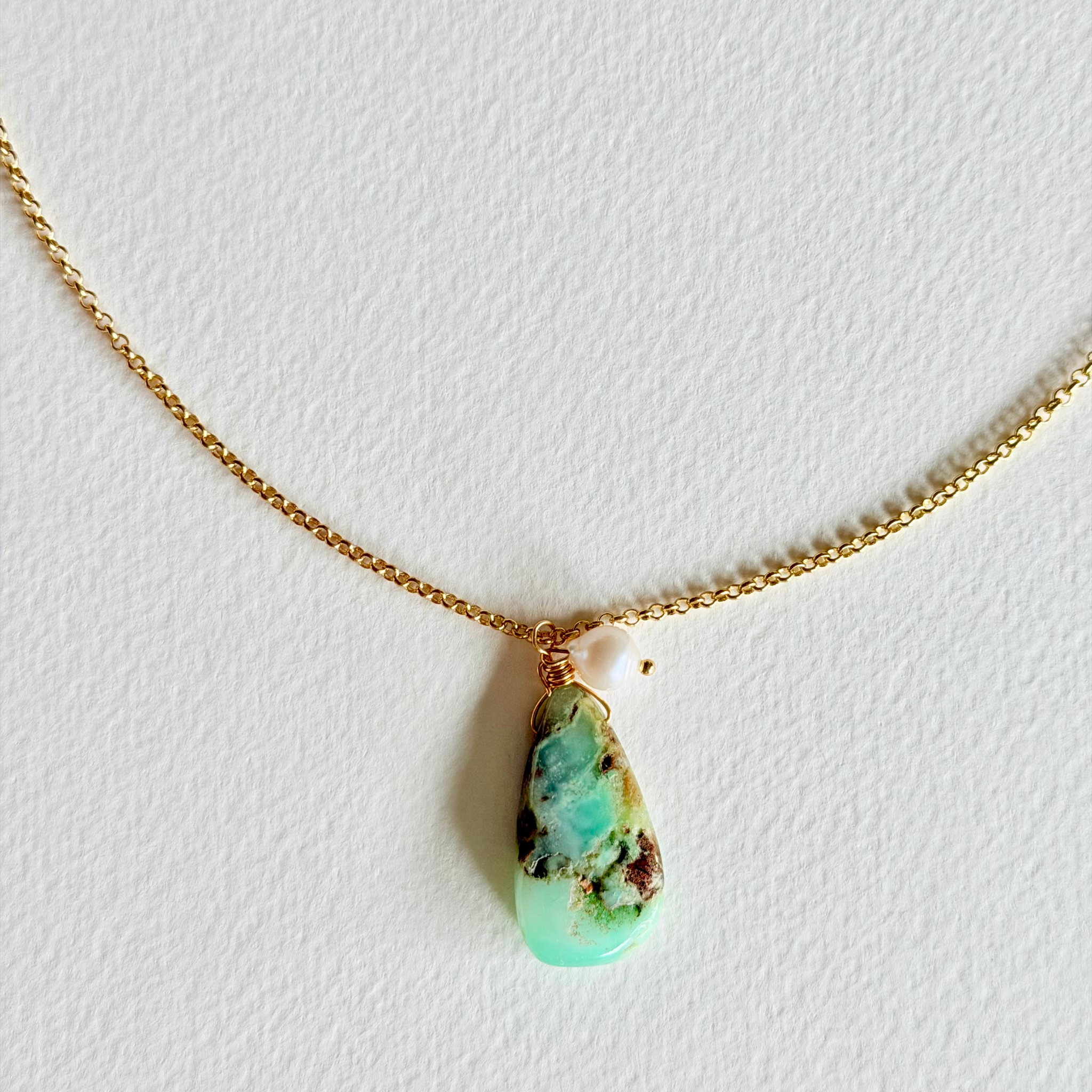 Turquoise pendant necklace on a gold chain against a white background
