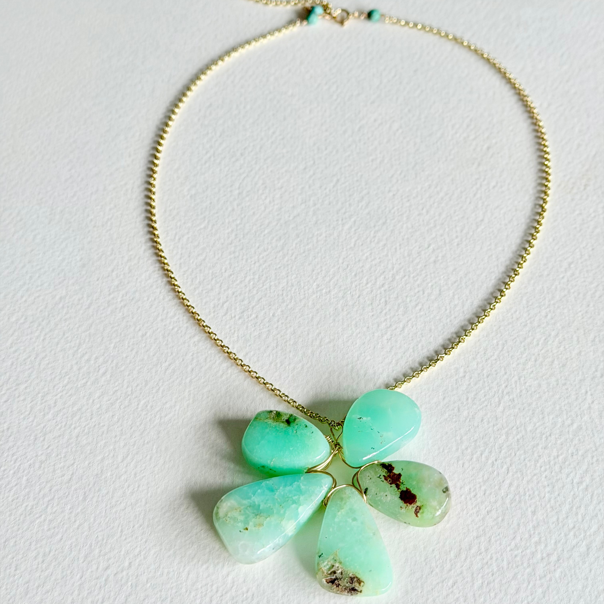 Necklace with a green chrysopace fllower shaped pendant on a light gray background
