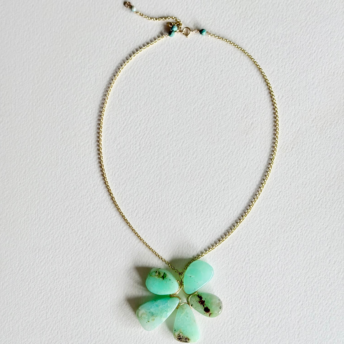 Necklace with a green flower-shaped pendant on a light gray background