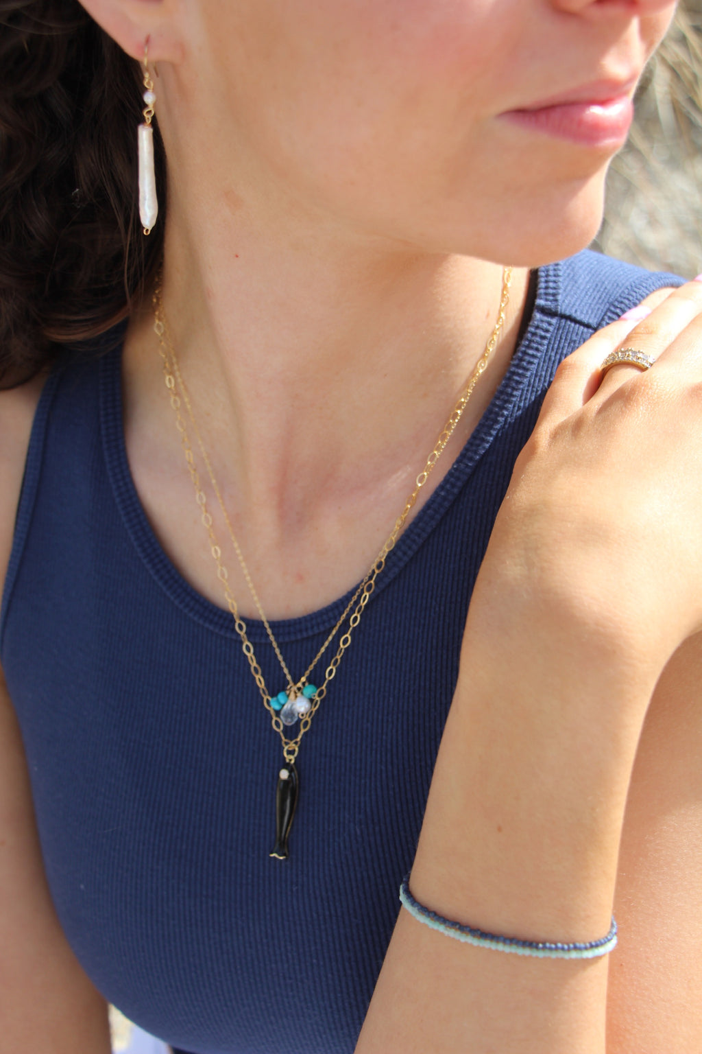 Close-up of a woman wearing a gold necklace with a pendant, blue top, and ring.