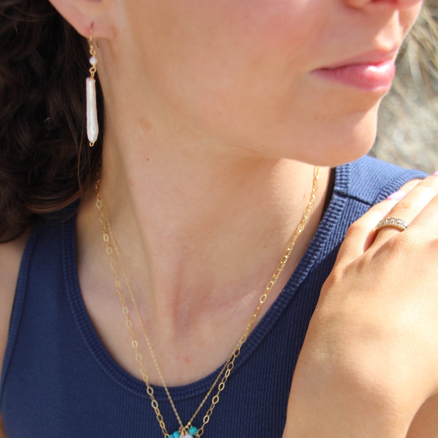 Close-up of a woman wearing a gold necklace with a pendant, blue top, and ring.