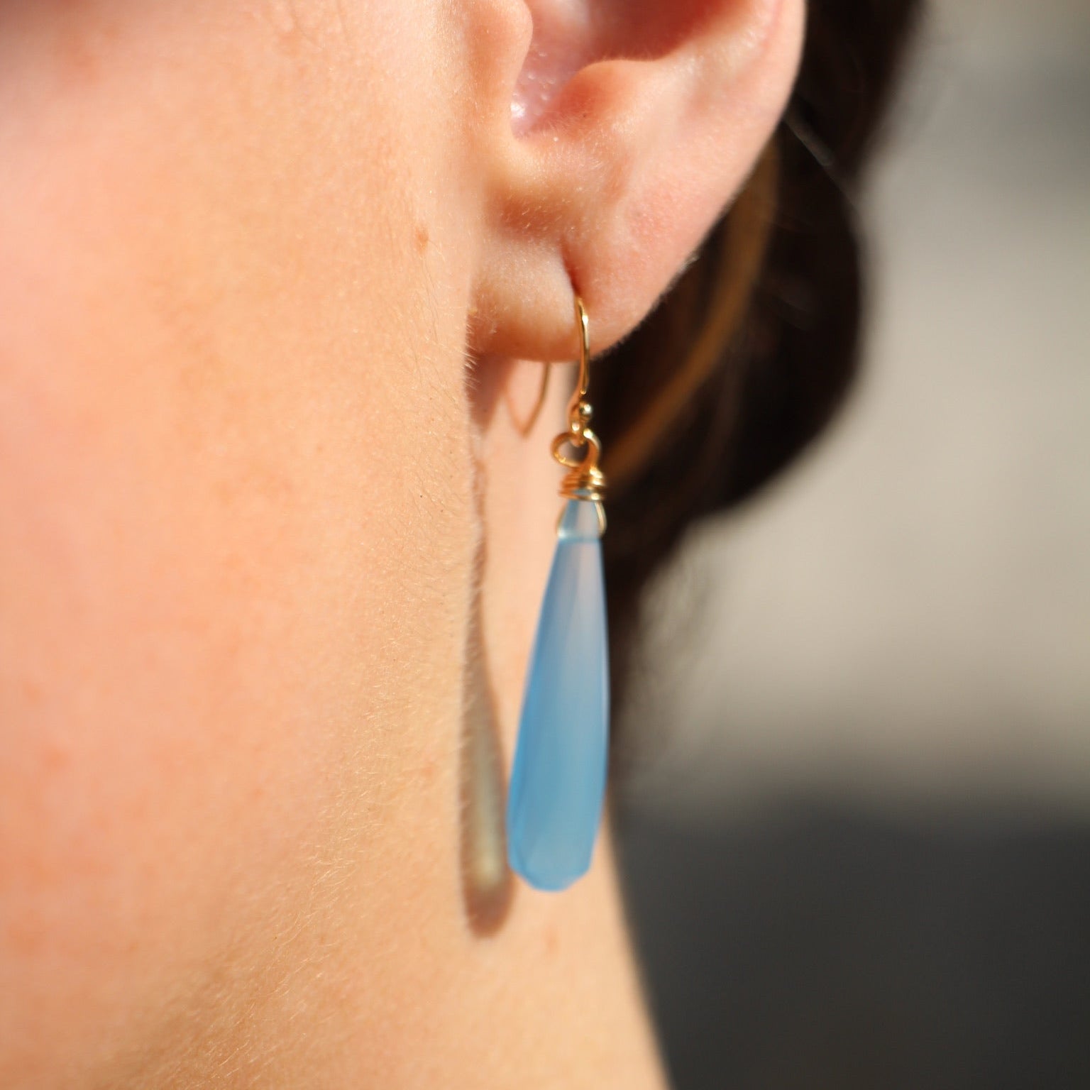 Close-up of an ear wearing a blue teardrop earring with a blurred background
