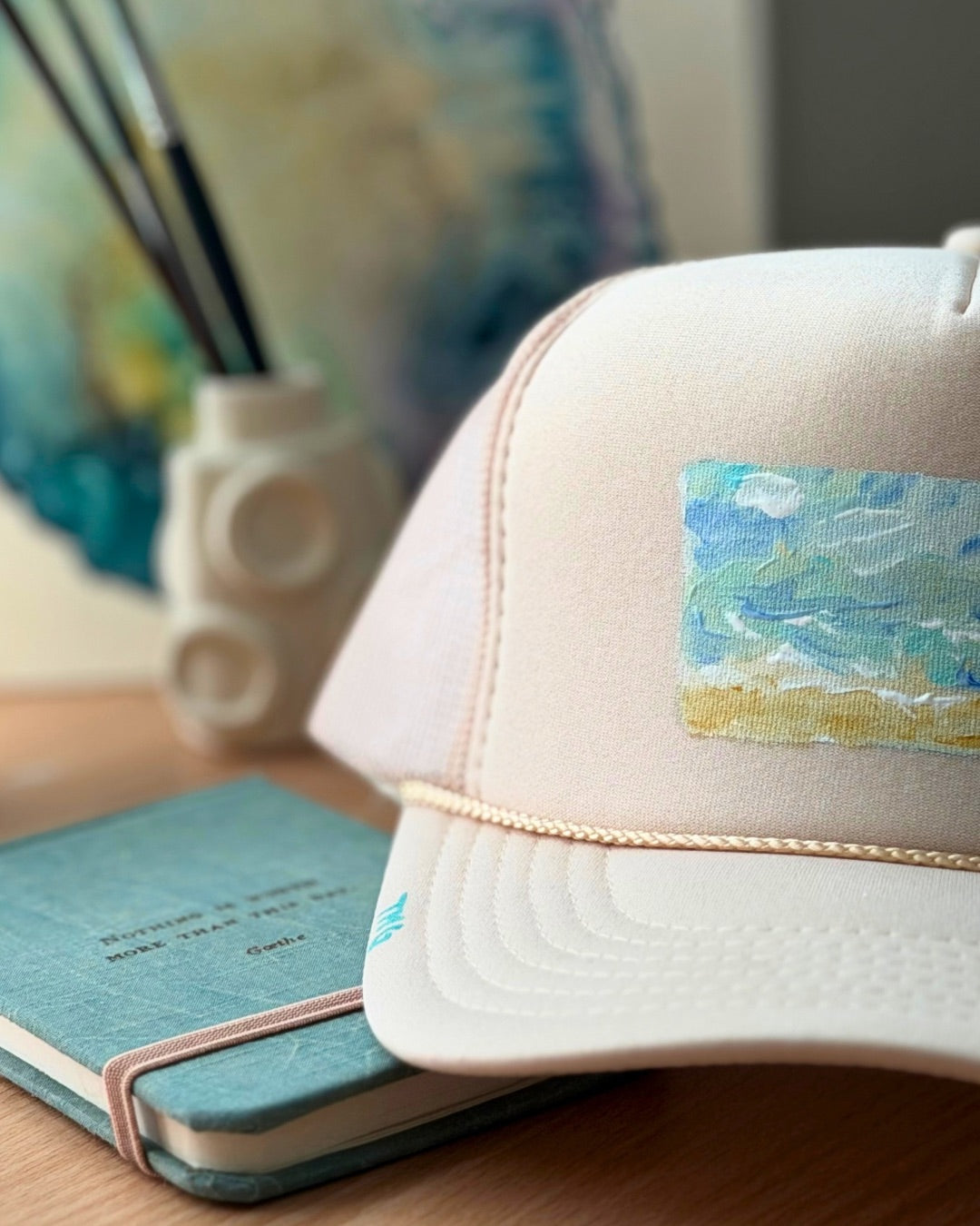 Cream hand-painted trucker hat featuring original textured ocean artwork in turquoise, blue and sandy gold by Marie & Oakley.