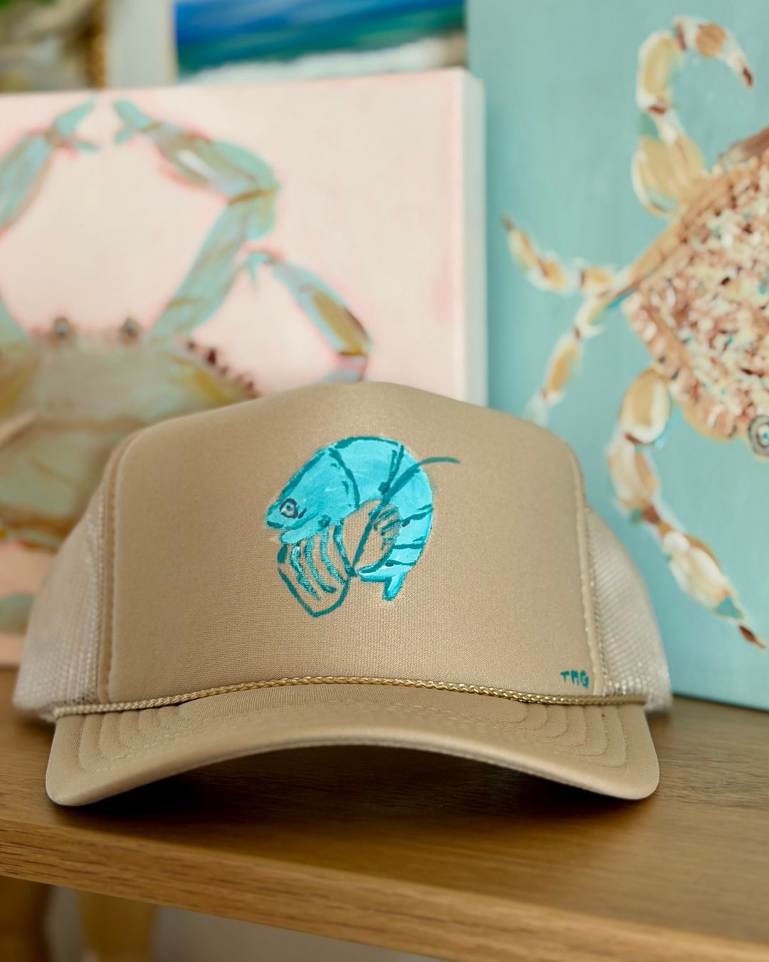 Khaki trucker hat featuring a whimsical hand-painted coastal shrimp in turquoise and aqua, original wearable art by Marie & Oakley.