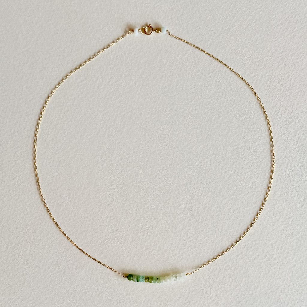 Gold necklace with a green pendant on a light gray background
