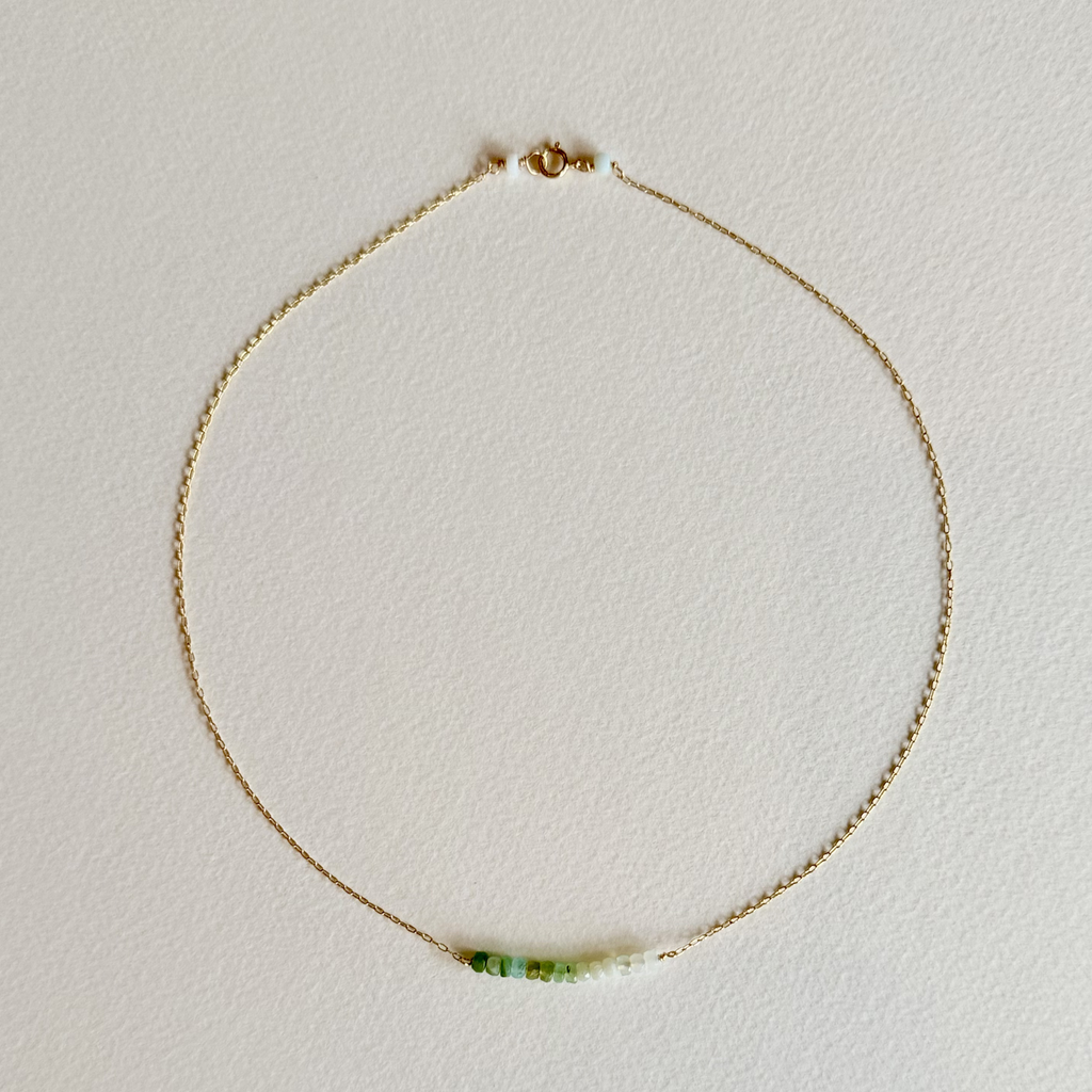 Gold necklace with a green gemstone on a light gray background