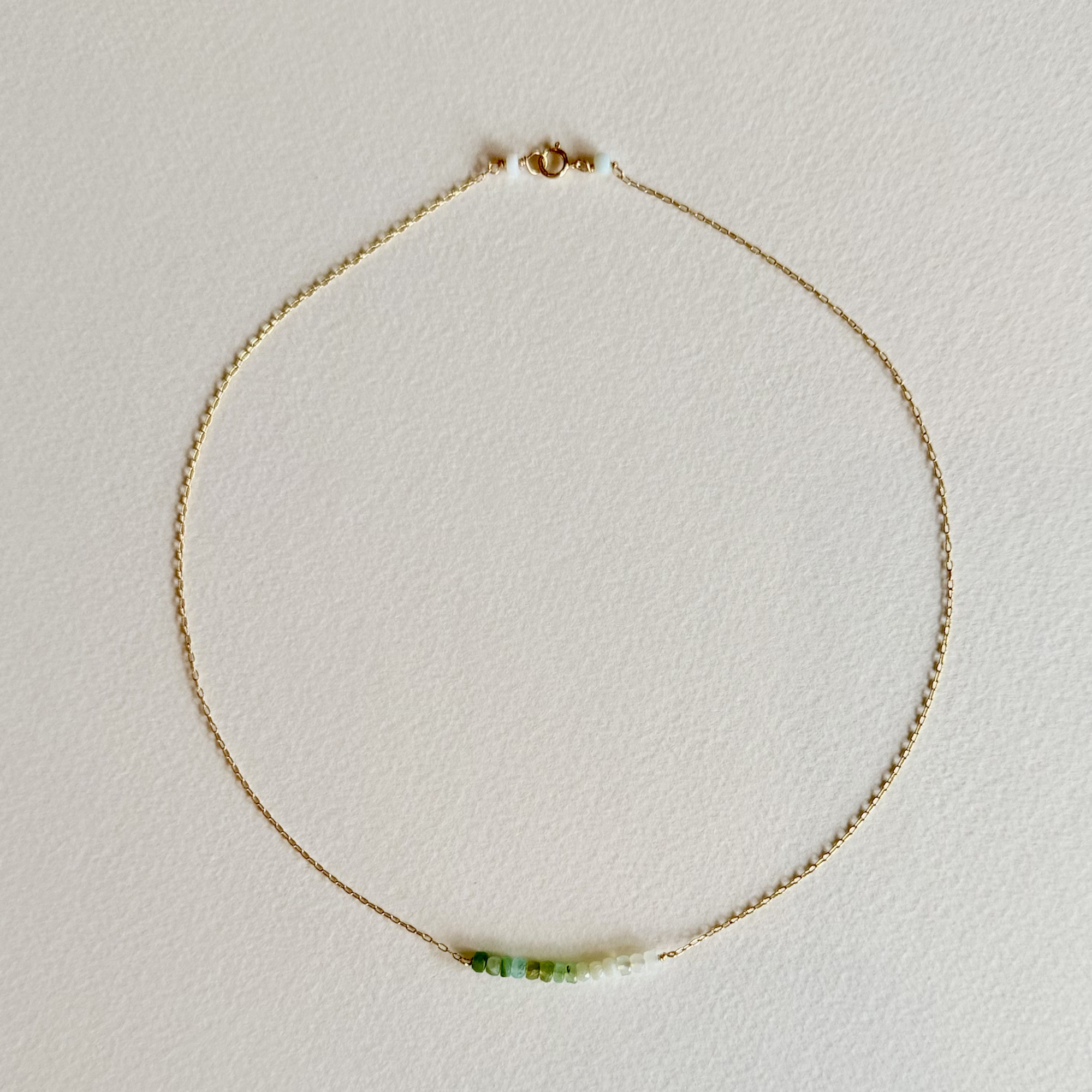 Gold necklace with a green gemstone on a light gray background