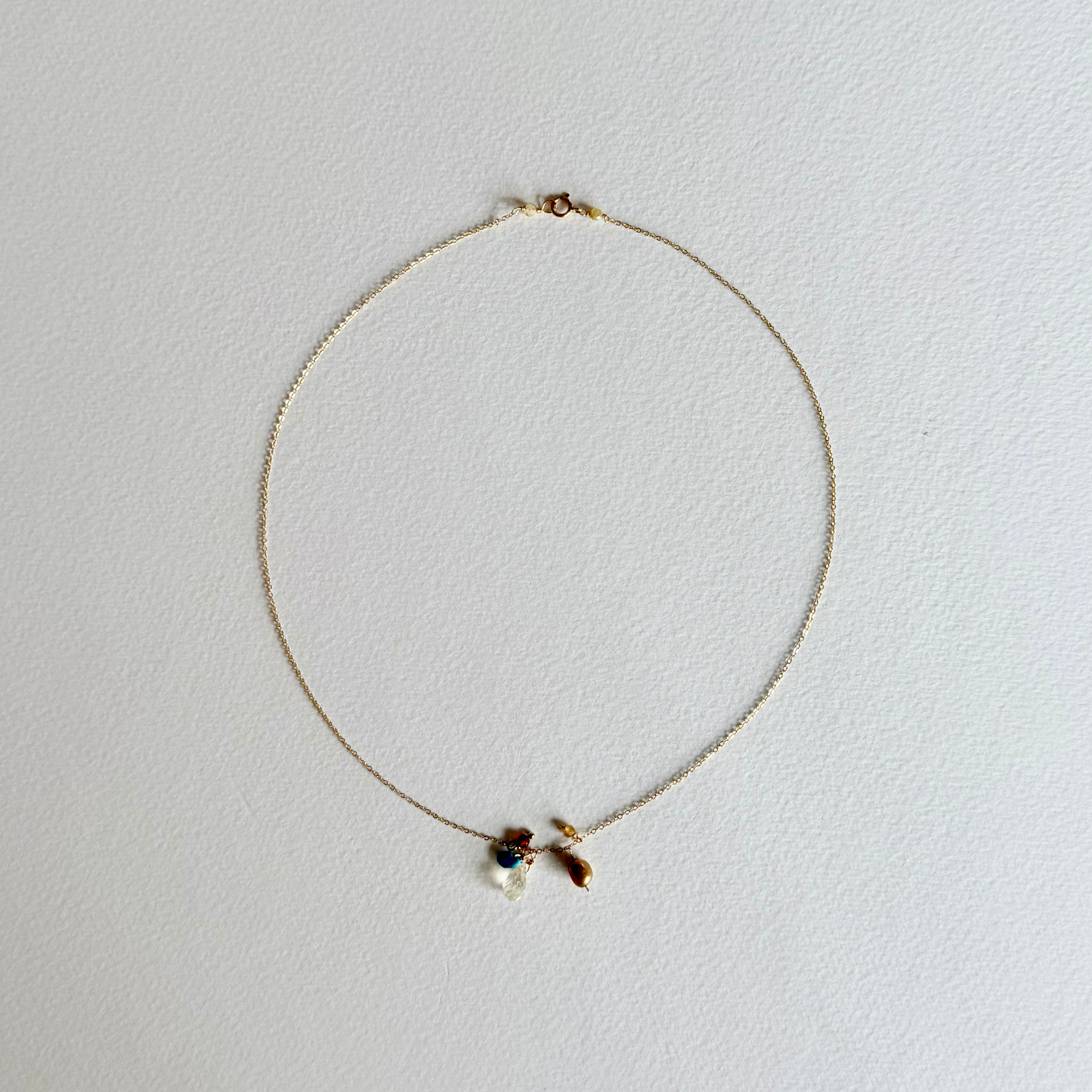 A delicate gold chain necklace with a small bow charm and a tiny blue bead accent, displayed on a textured white background.