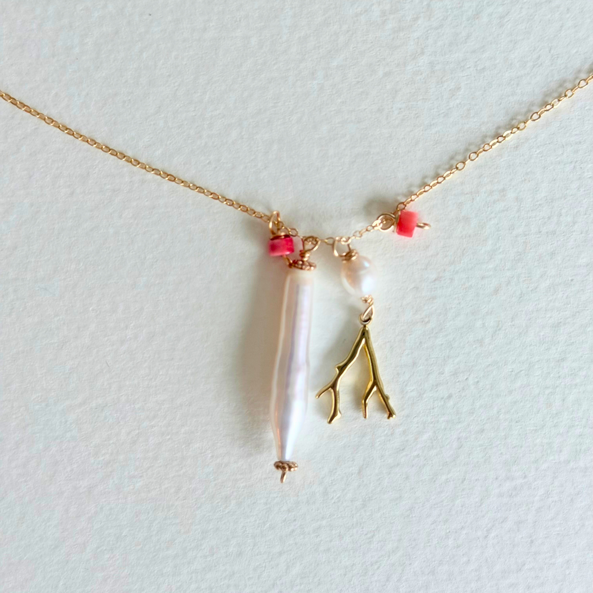 Necklace with a pearl pendant and gold branch charm on a light background