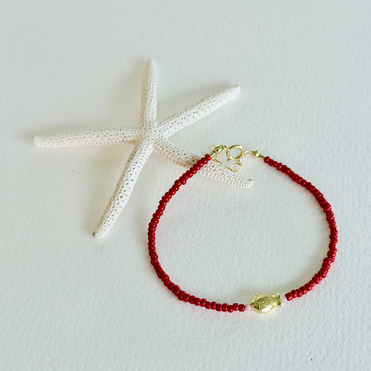 Red beaded bracelet with a gold clasp on a white background with a starfish.