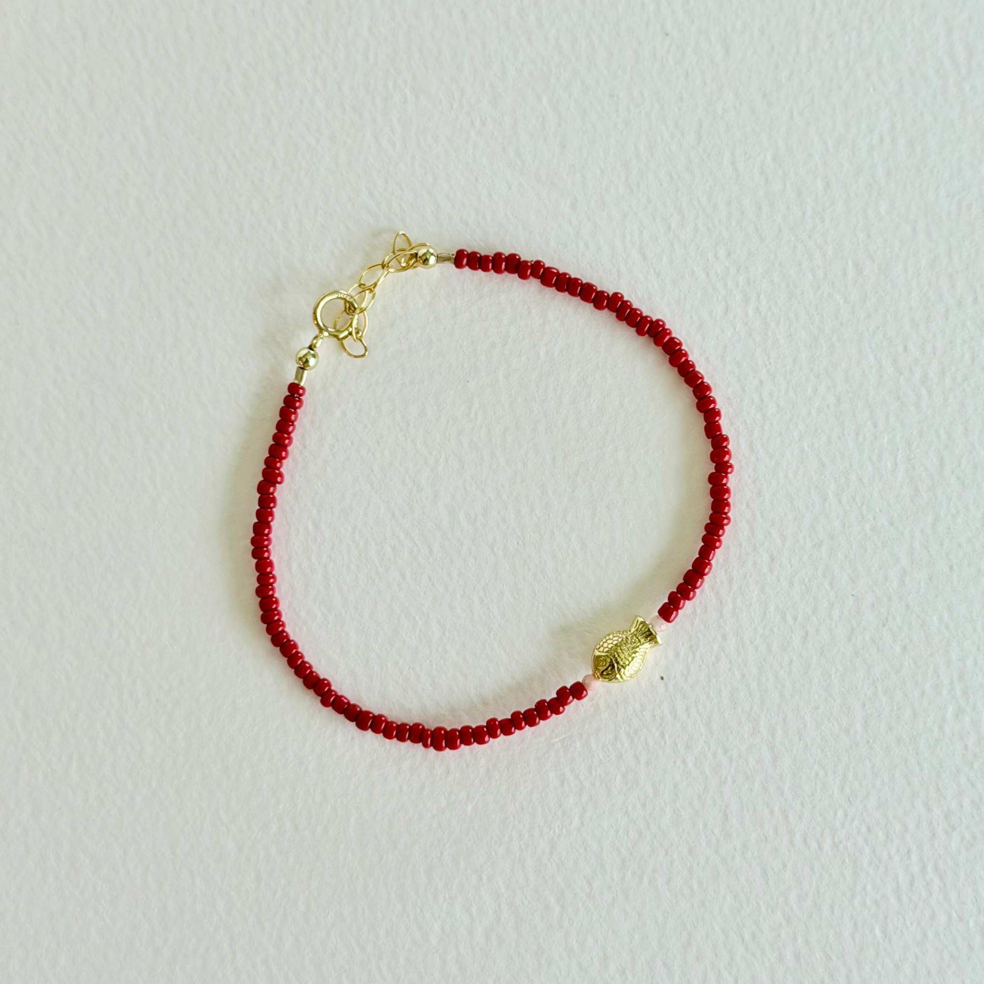 Red beaded bracelet with a gold clasp on a light gray background