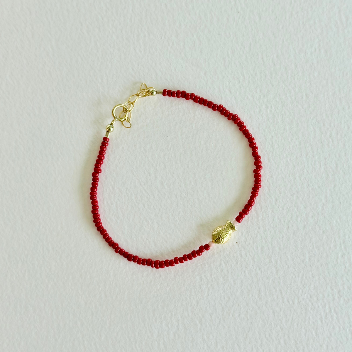 Red beaded bracelet with a gold clasp on a light gray background